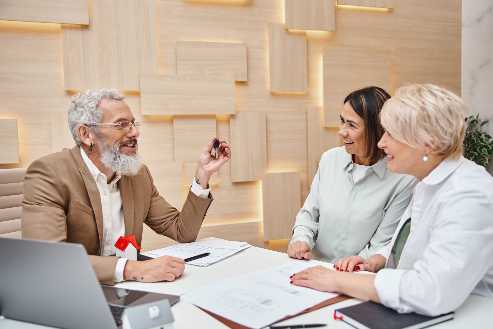 Three people in a meeting, discussing documents at a desk in a bright office