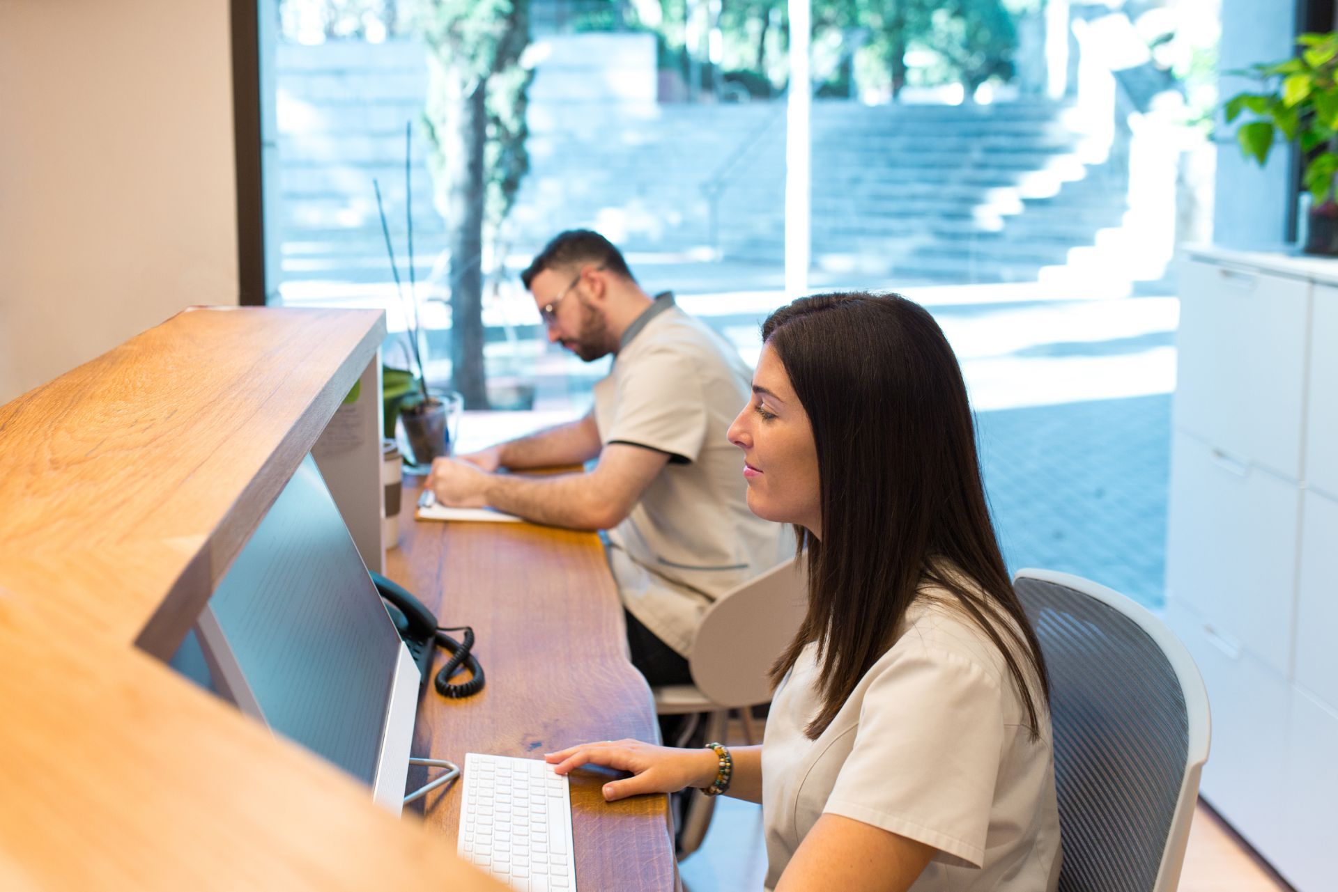 Two people working at a wooden reception desk in a bright office lobby