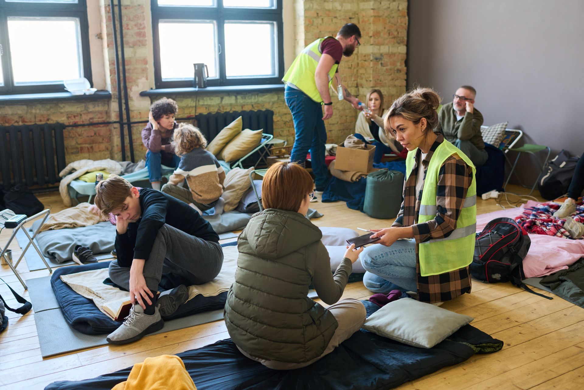People sitting and unpacking gear on mats in a bright indoor room, with bags and blankets around them.