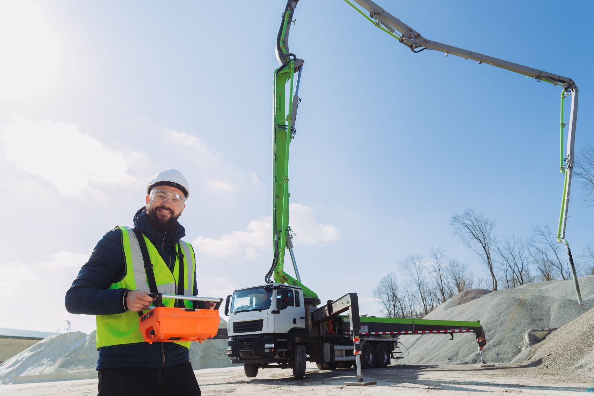 Worker in neon safety vest operating a boom pump truck on a construction site under a clear blue sky