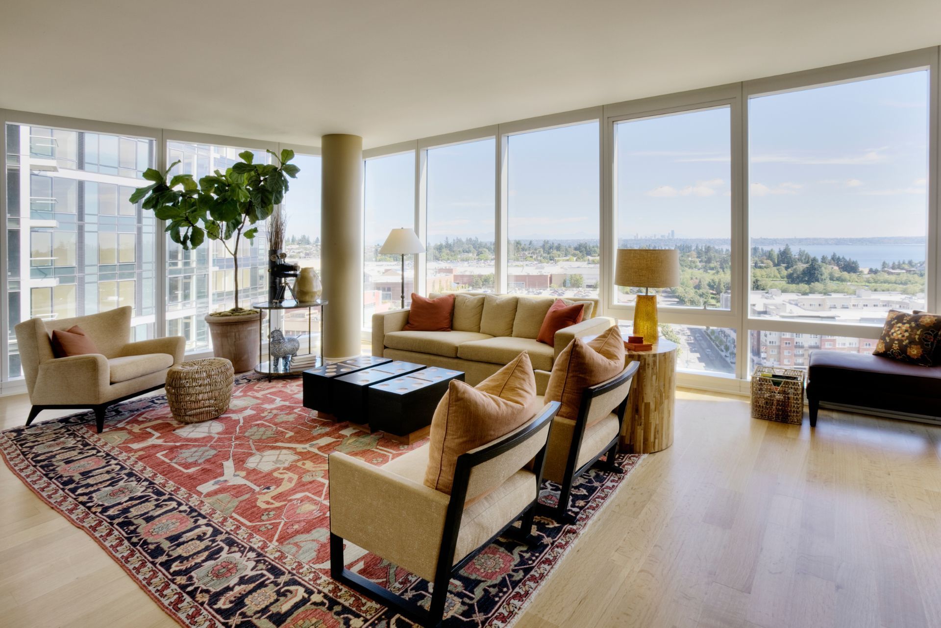 Bright living room with large windows, patterned rug, tan chairs, and city and water views