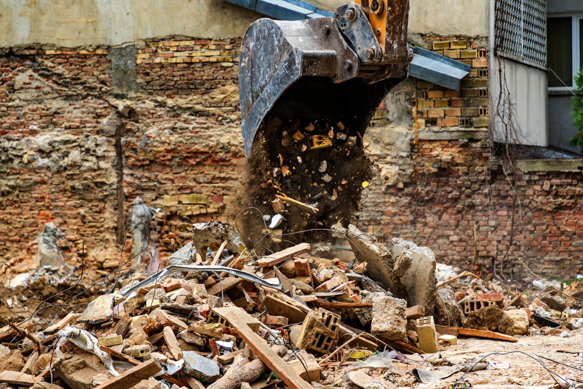 Excavator dumping rubble beside a crumbling brick wall at a demolition site