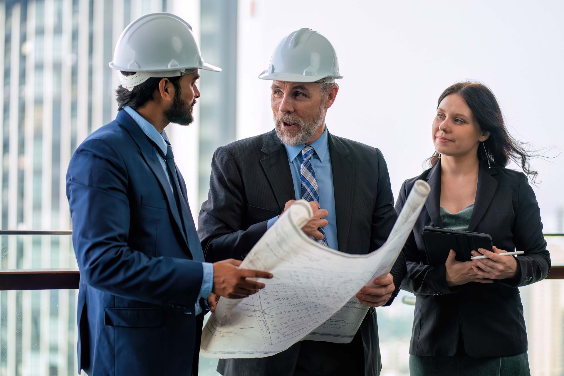 Three construction workers in hard hats discuss blueprints at a building site
