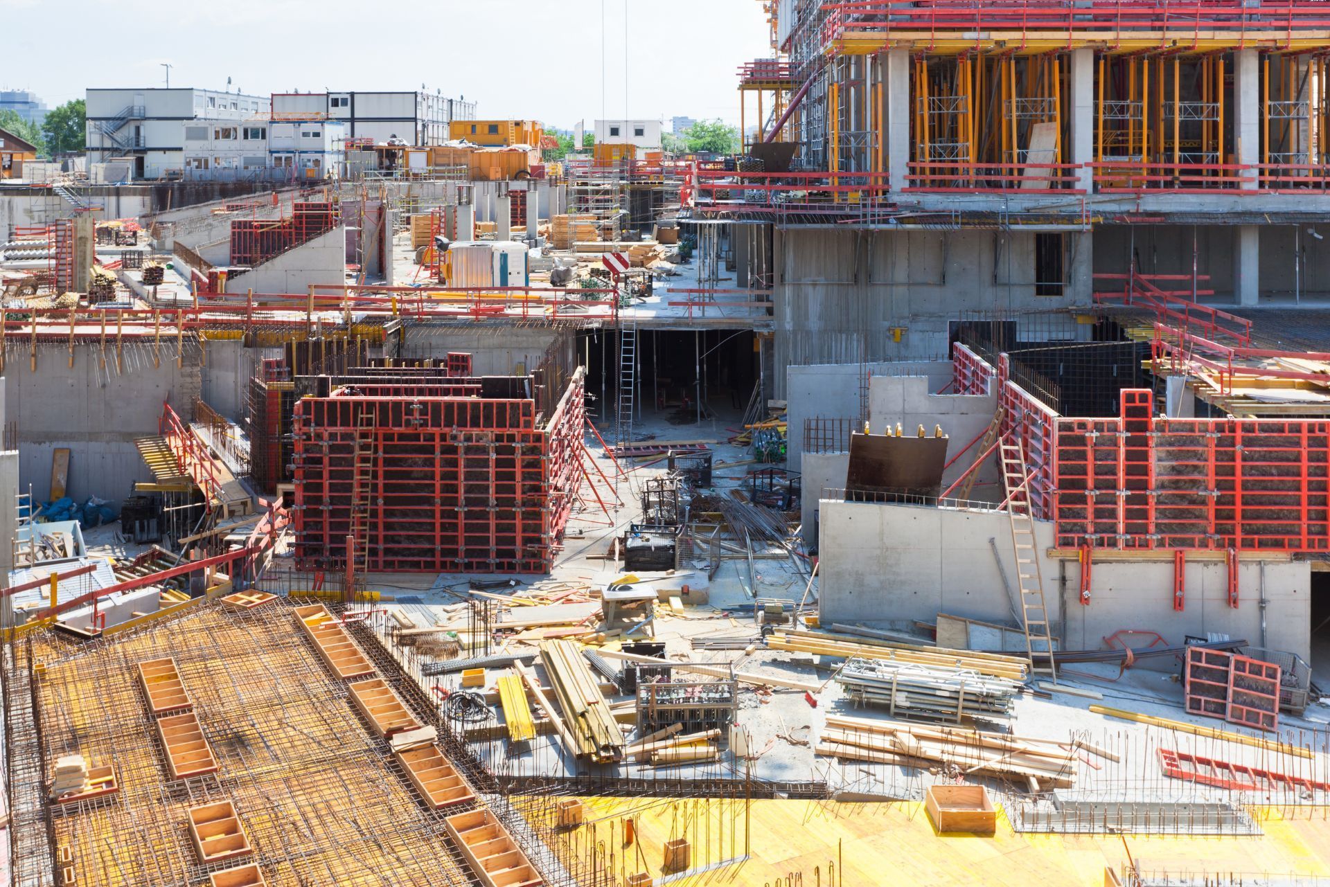 Construction site with red scaffolding, concrete structures, and building materials scattered across the ground
