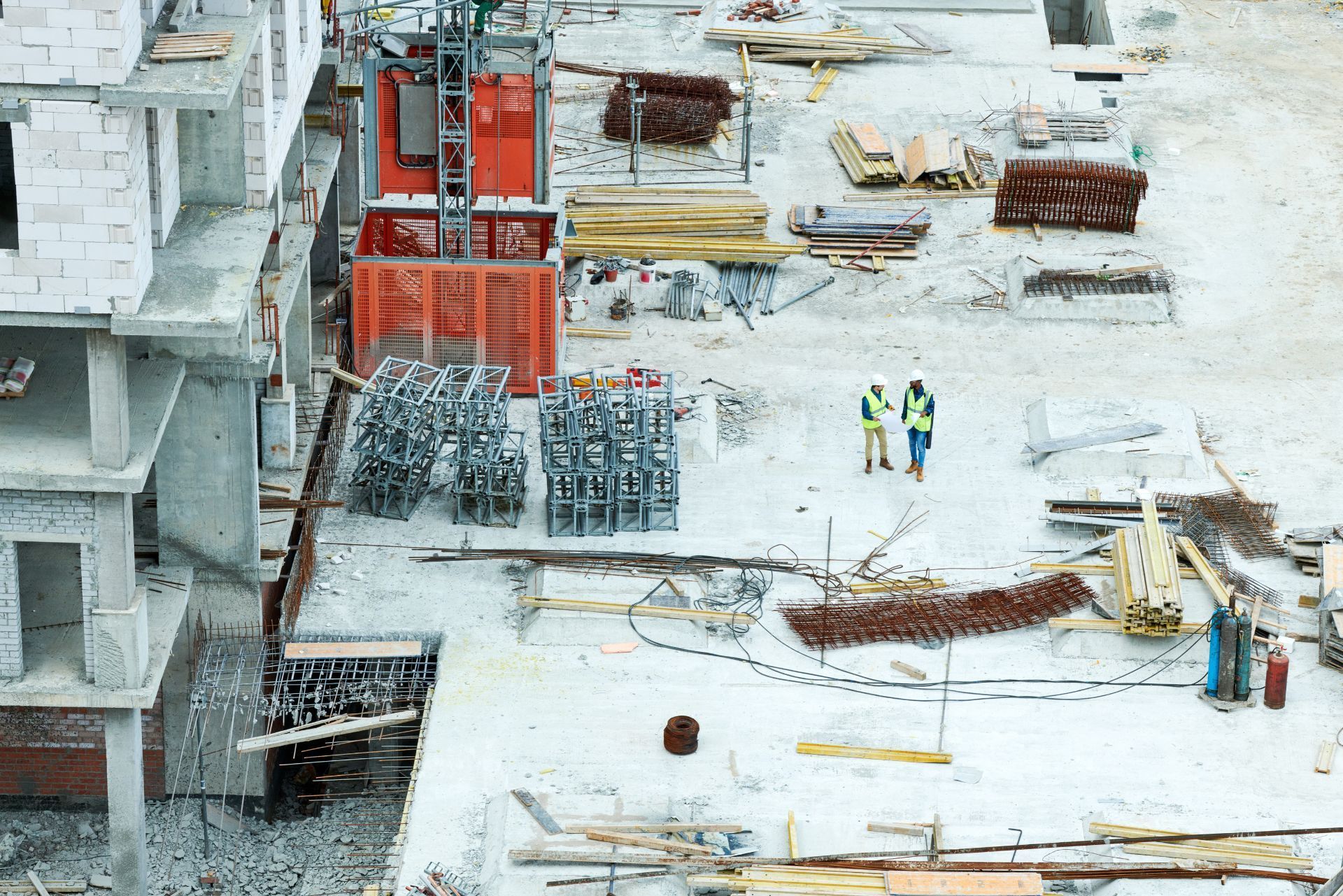 Construction site with workers in neon vests, steel rebar, and red formwork on a snowy ground