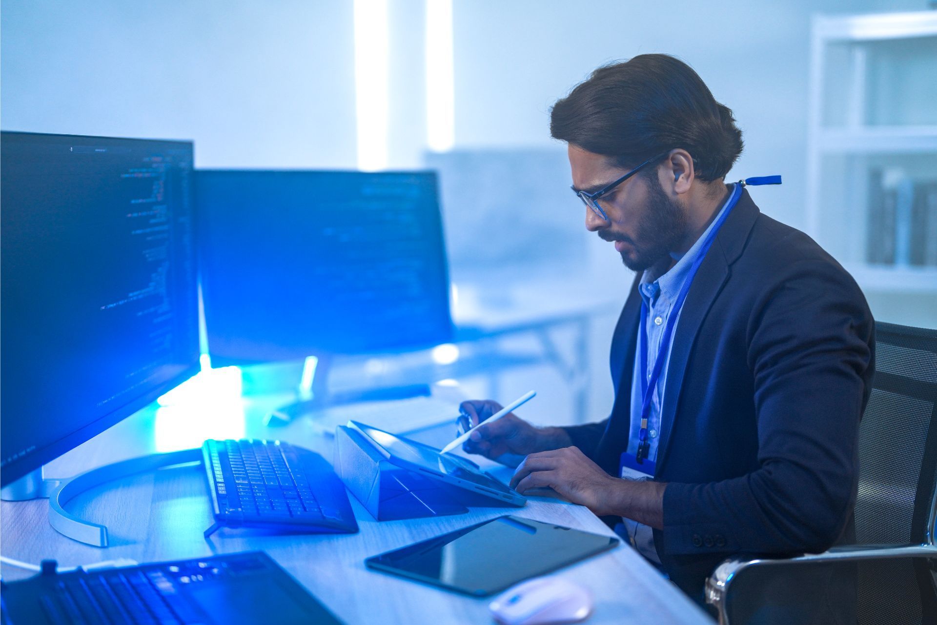 Person working at a desk with laptop and monitors in a blue-lit office