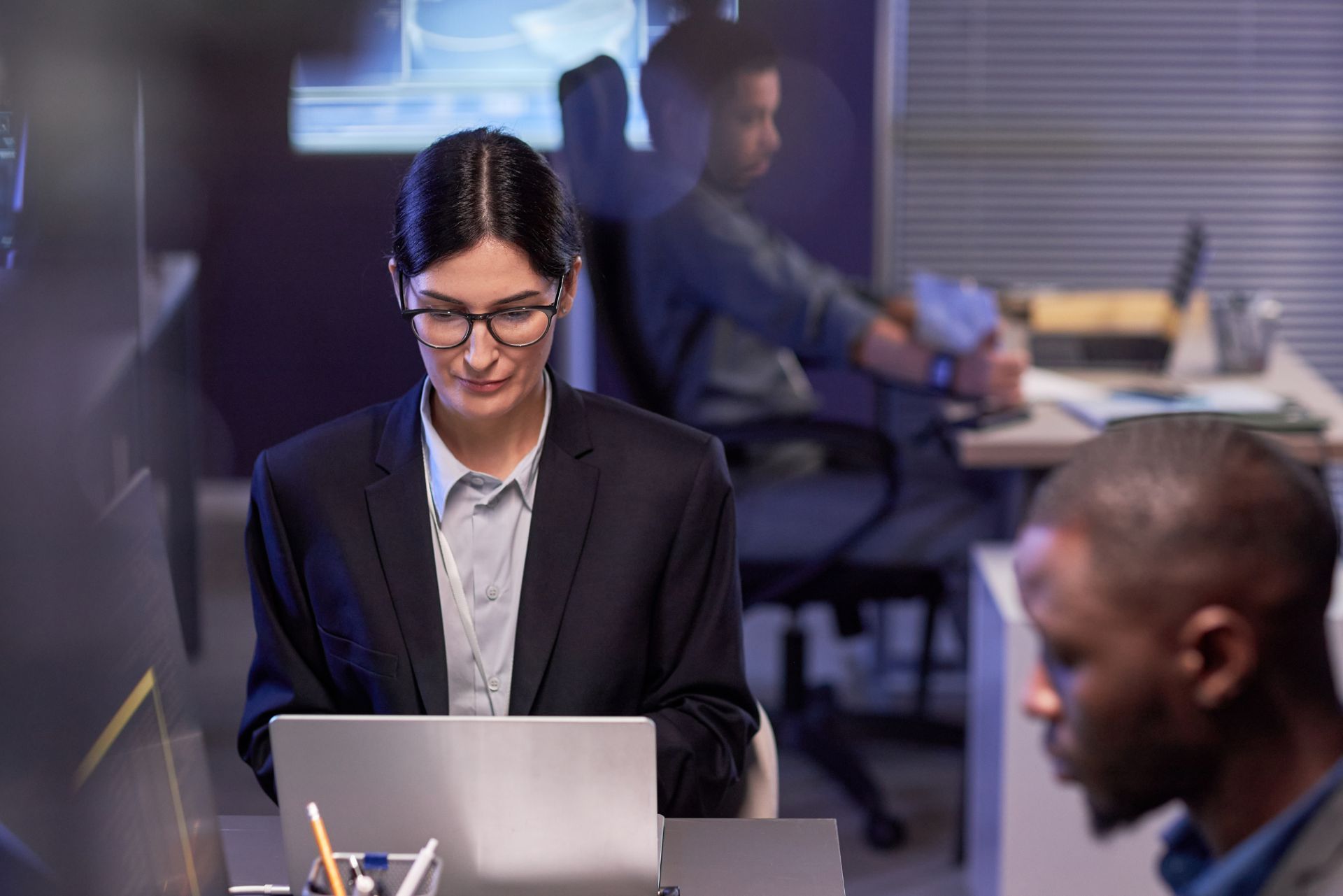 People working in a modern office, with a woman focused on her laptop in the foreground.
