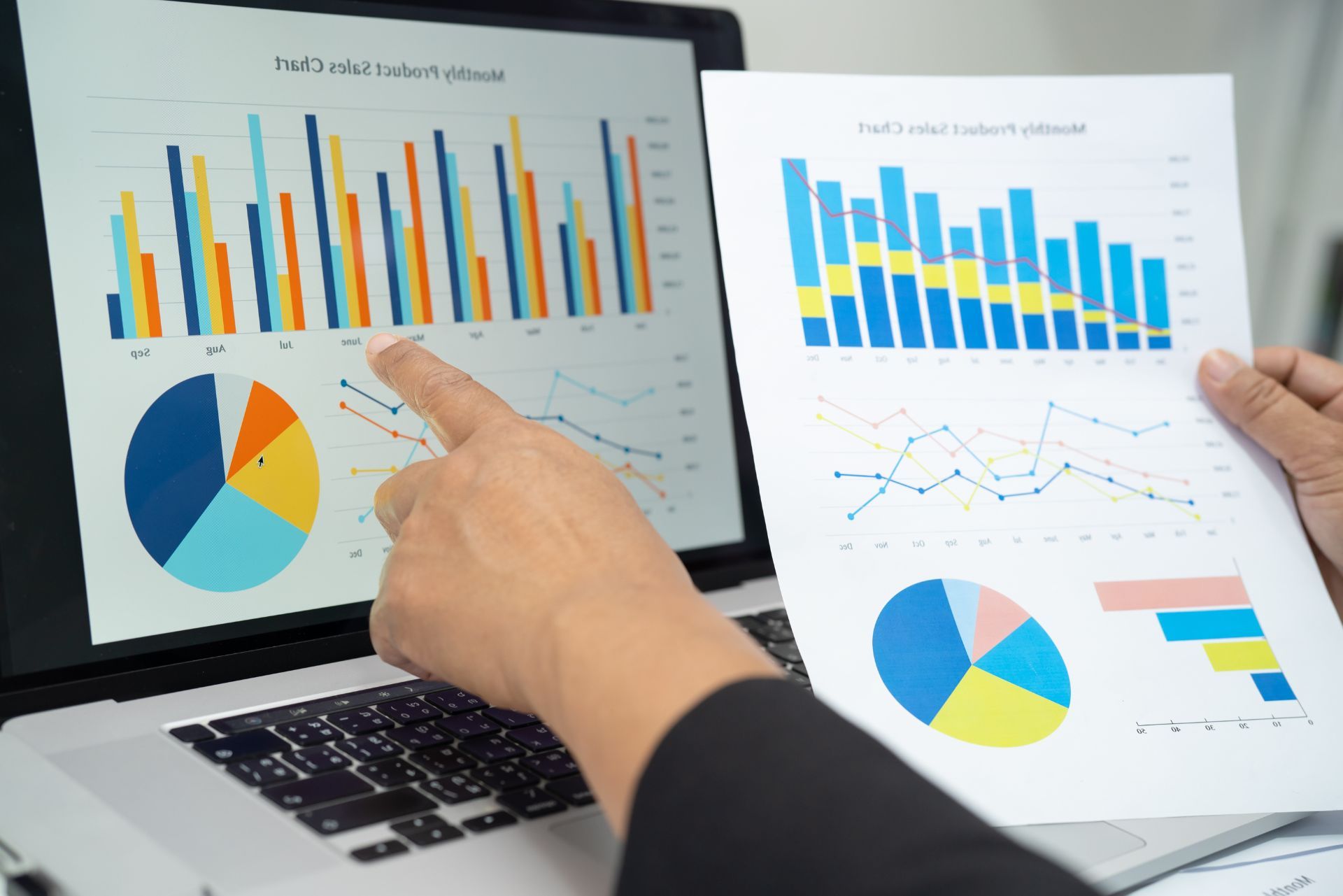 Hand pointing at charts on a laptop and printed reports with bar and pie graphs