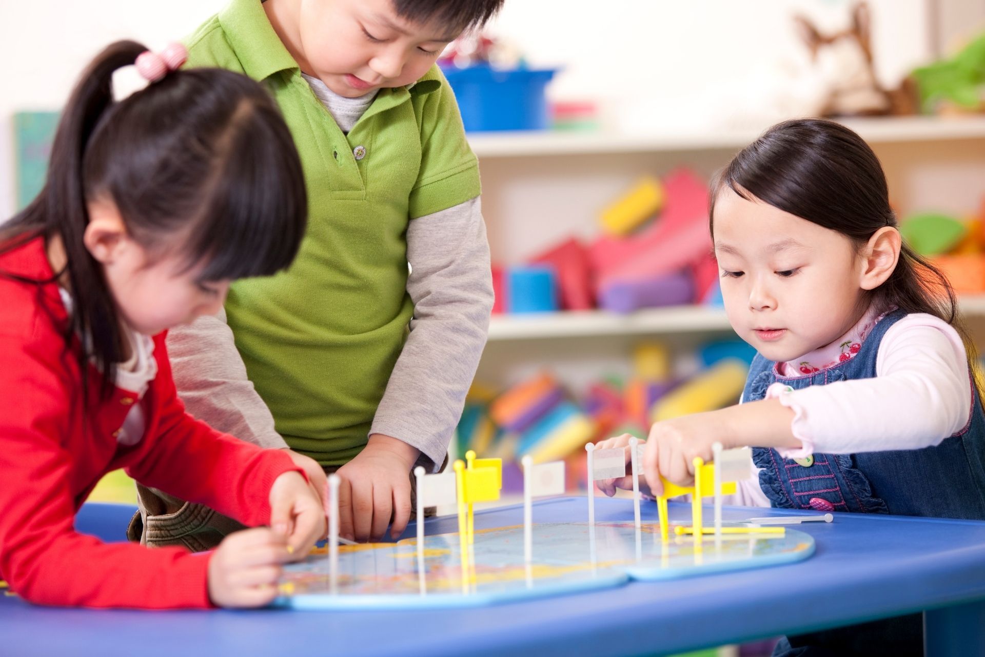 Three children play a colorful tabletop game in a classroom setting