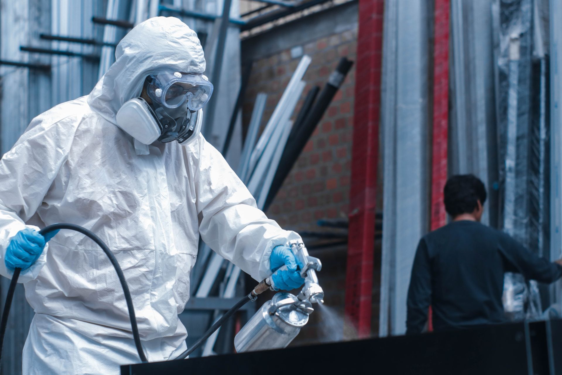 Worker in white protective suit and mask spray-painting near a building.