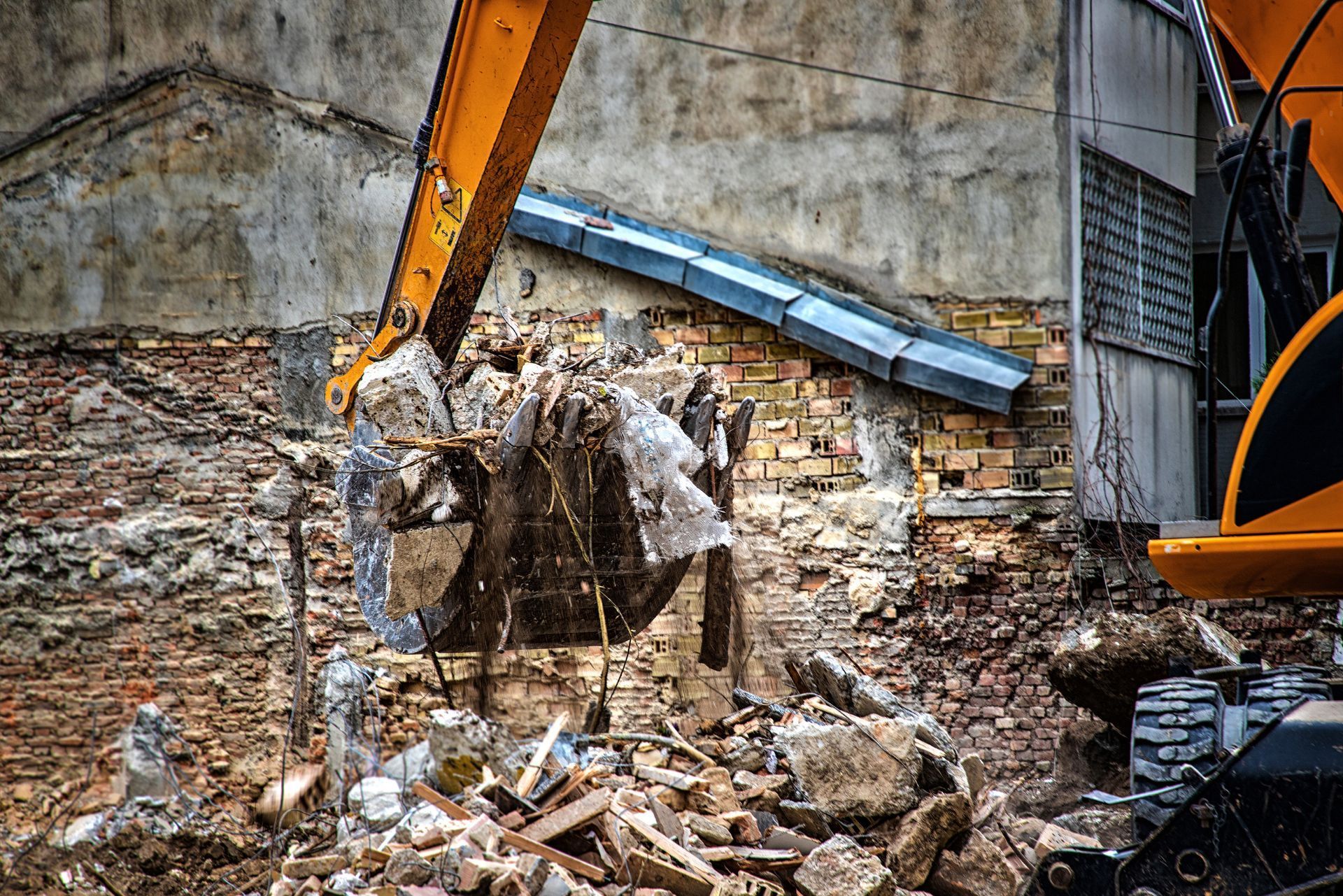 Yellow excavator digging into a pile of rubble and debris at a construction or demolition site.