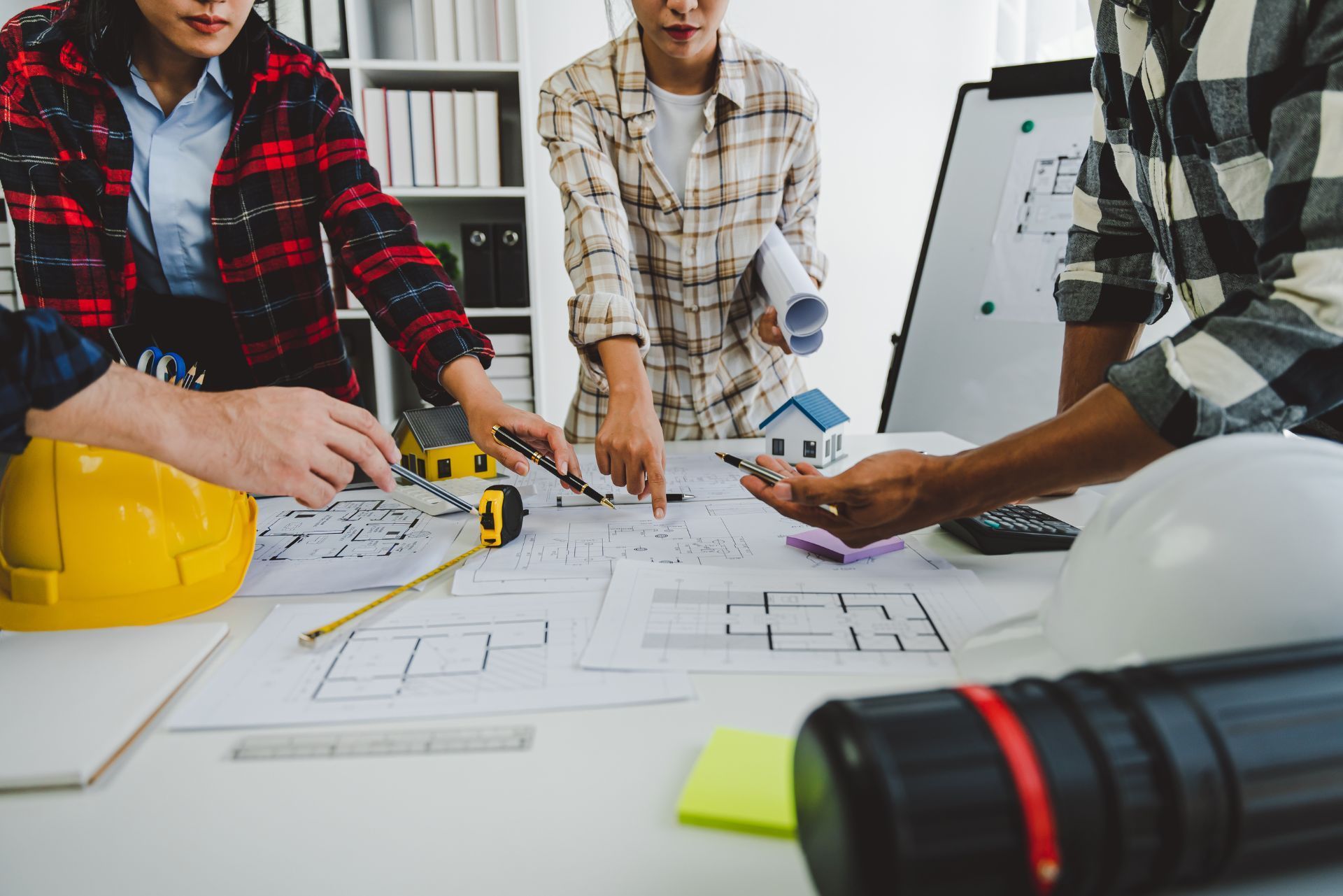 Workers reviewing blueprints and tools at a construction planning table with hard hats and laptop