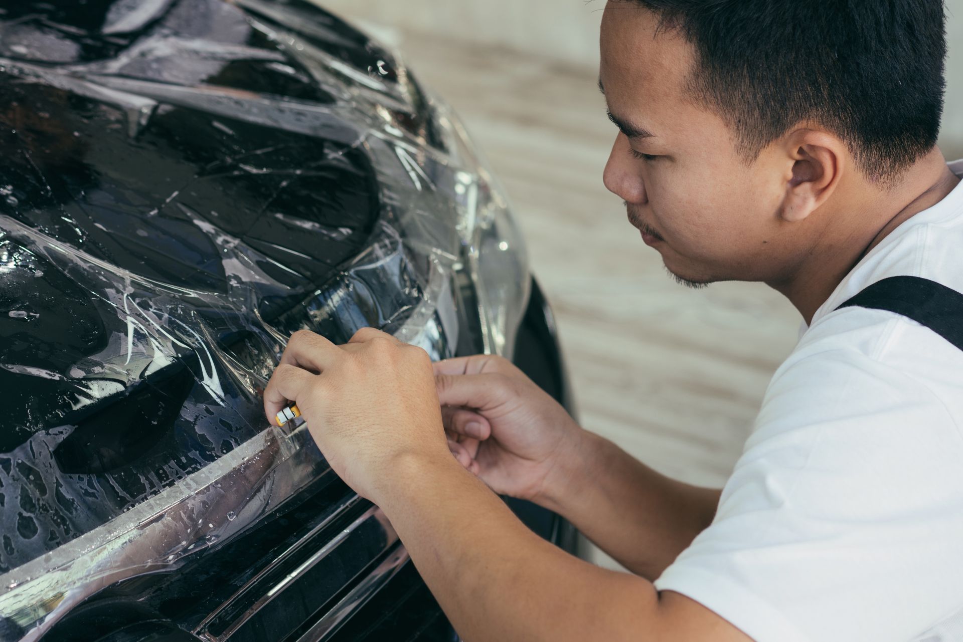 Person applying clear protective film to a car bumper indoors
