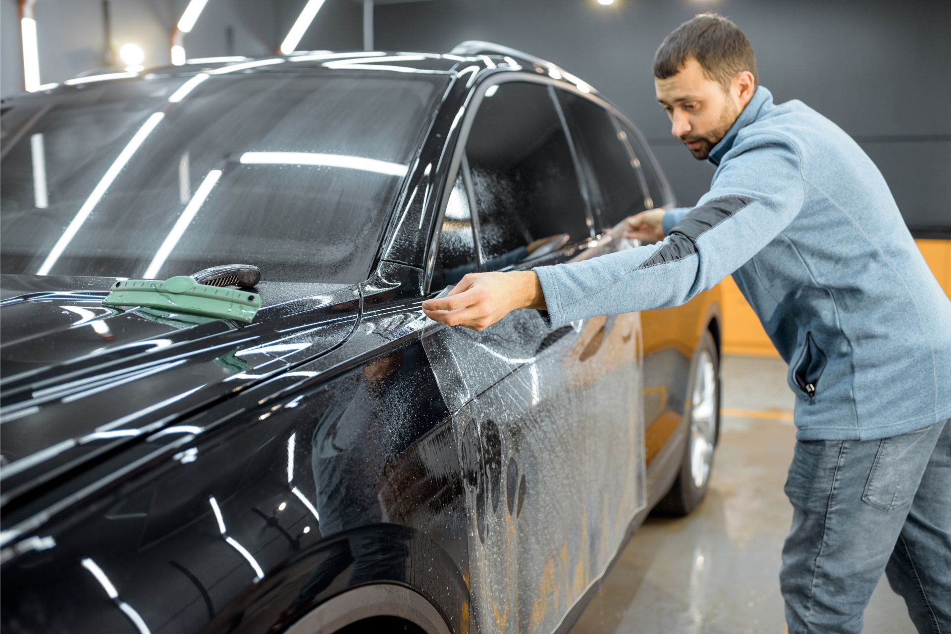 Man washing a black car in a garage, wiping the side with a cloth.