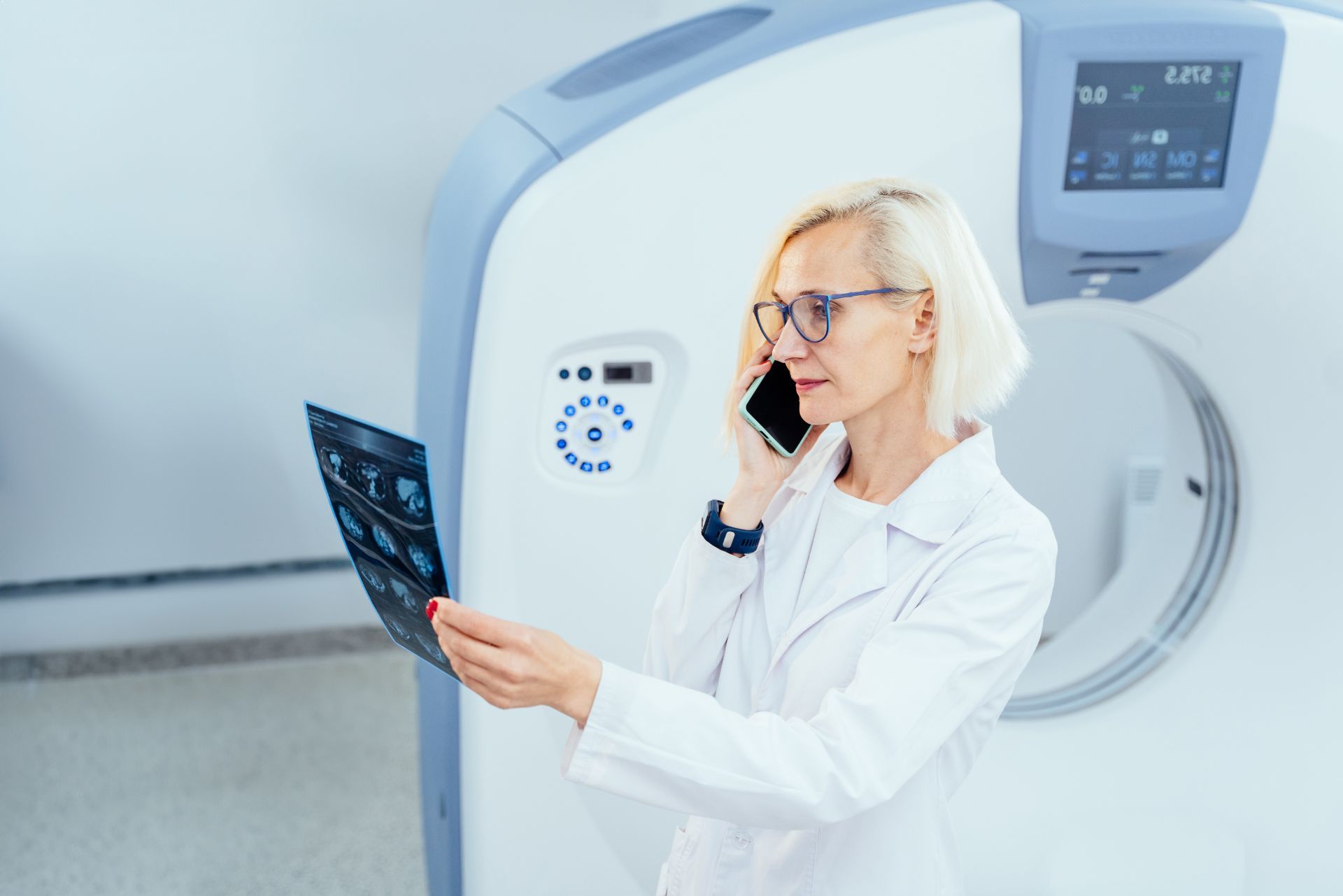 Doctor reviewing a chest X-ray while talking on a phone beside a CT scanner