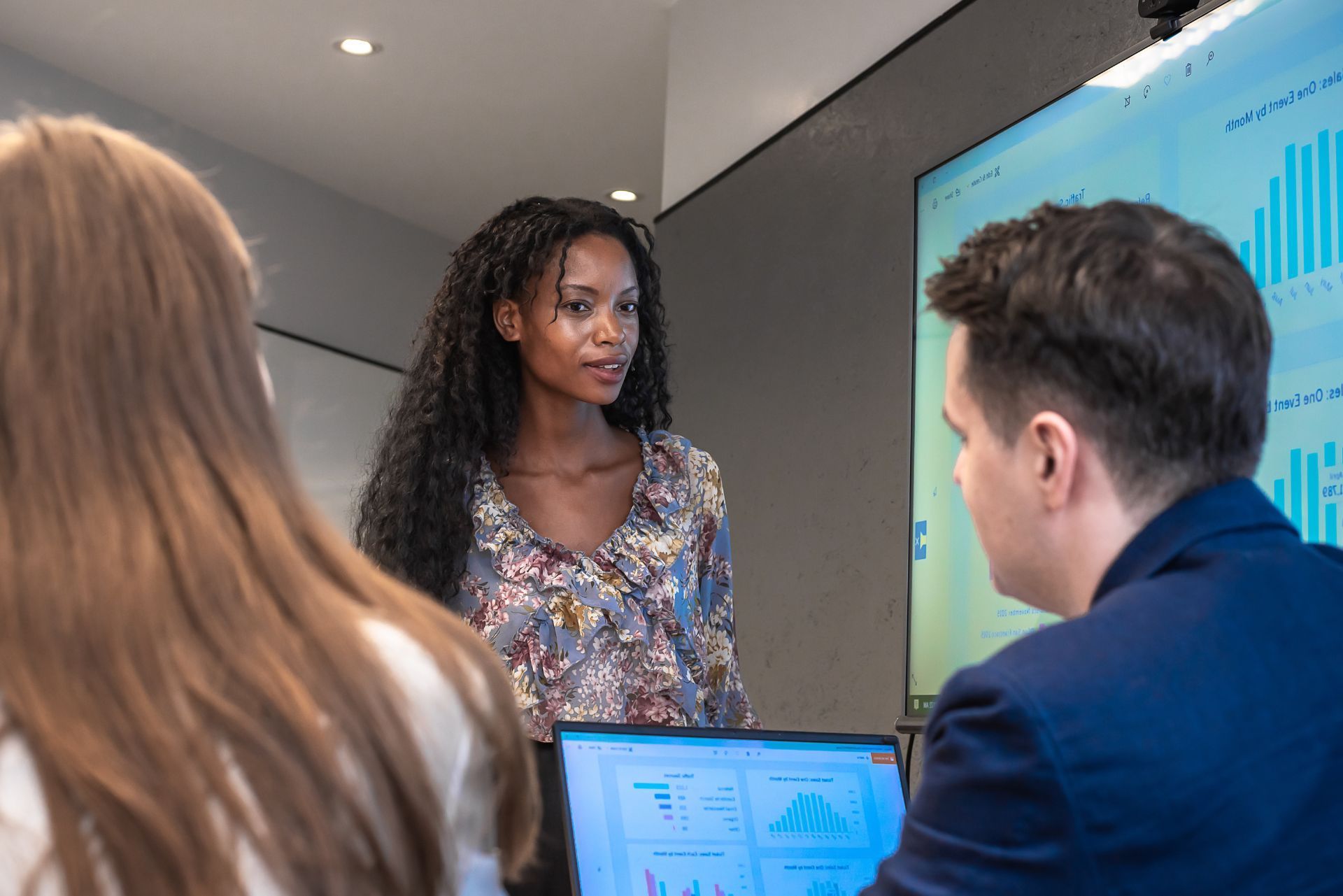 Team meeting in a conference room, with a presenter beside a screen and two people listening.