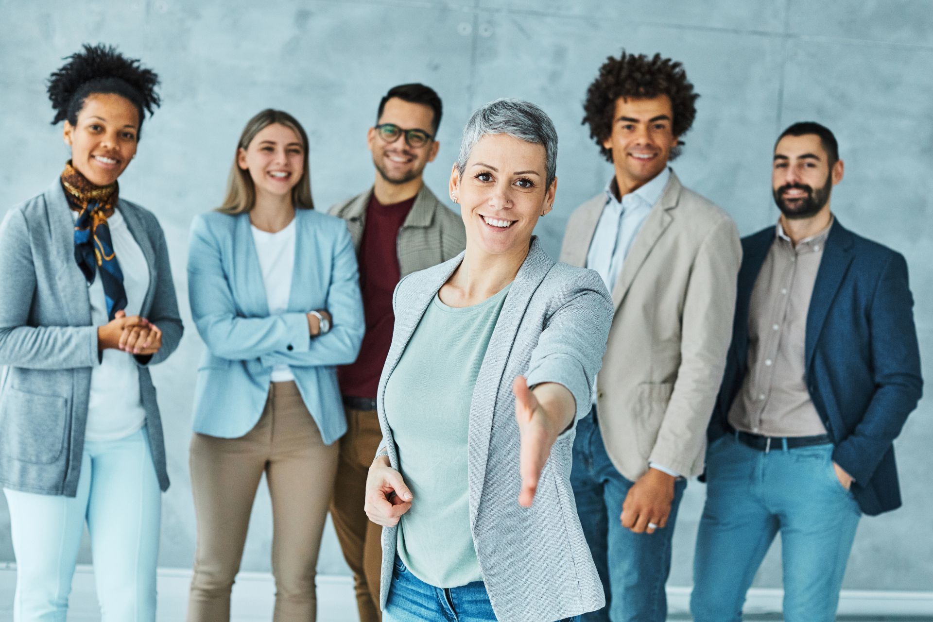 Group of six coworkers standing together in a bright office, smiling at the camera.