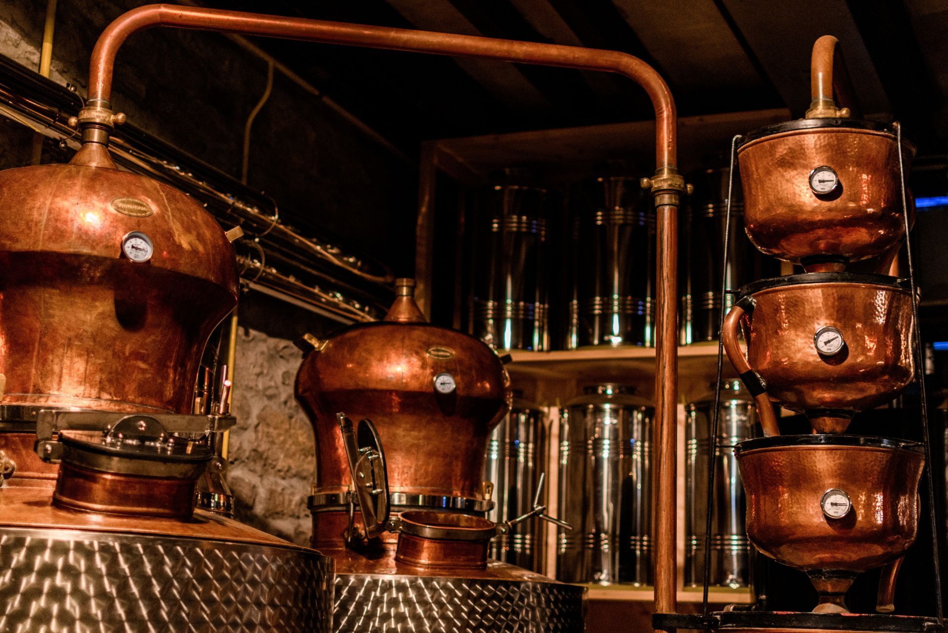 Shiny copper stills and distillation equipment set up in a dimly lit, industrial workshop.