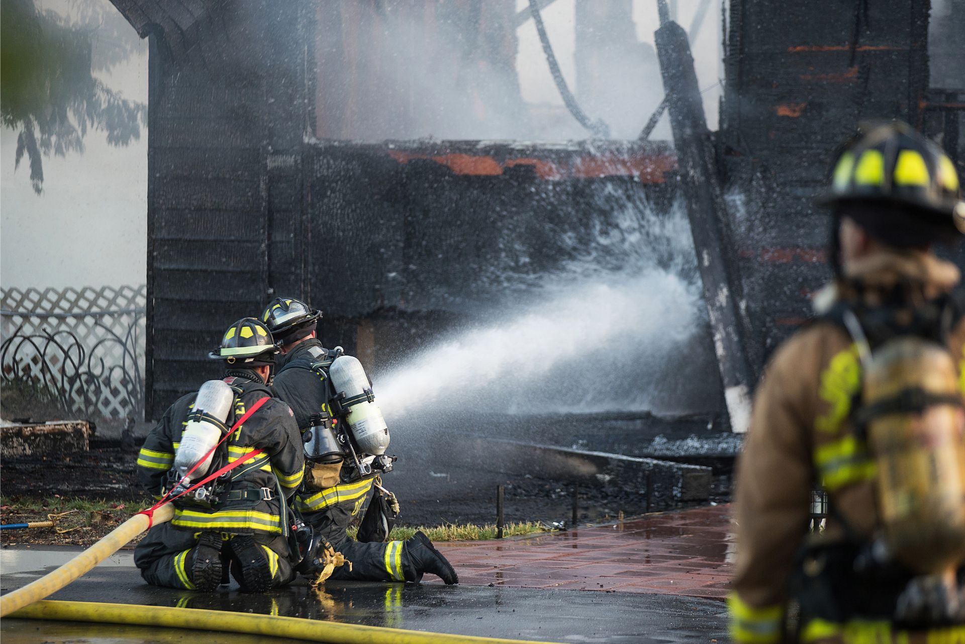 Firefighters spraying water on a burning building, with smoke and flames in the background