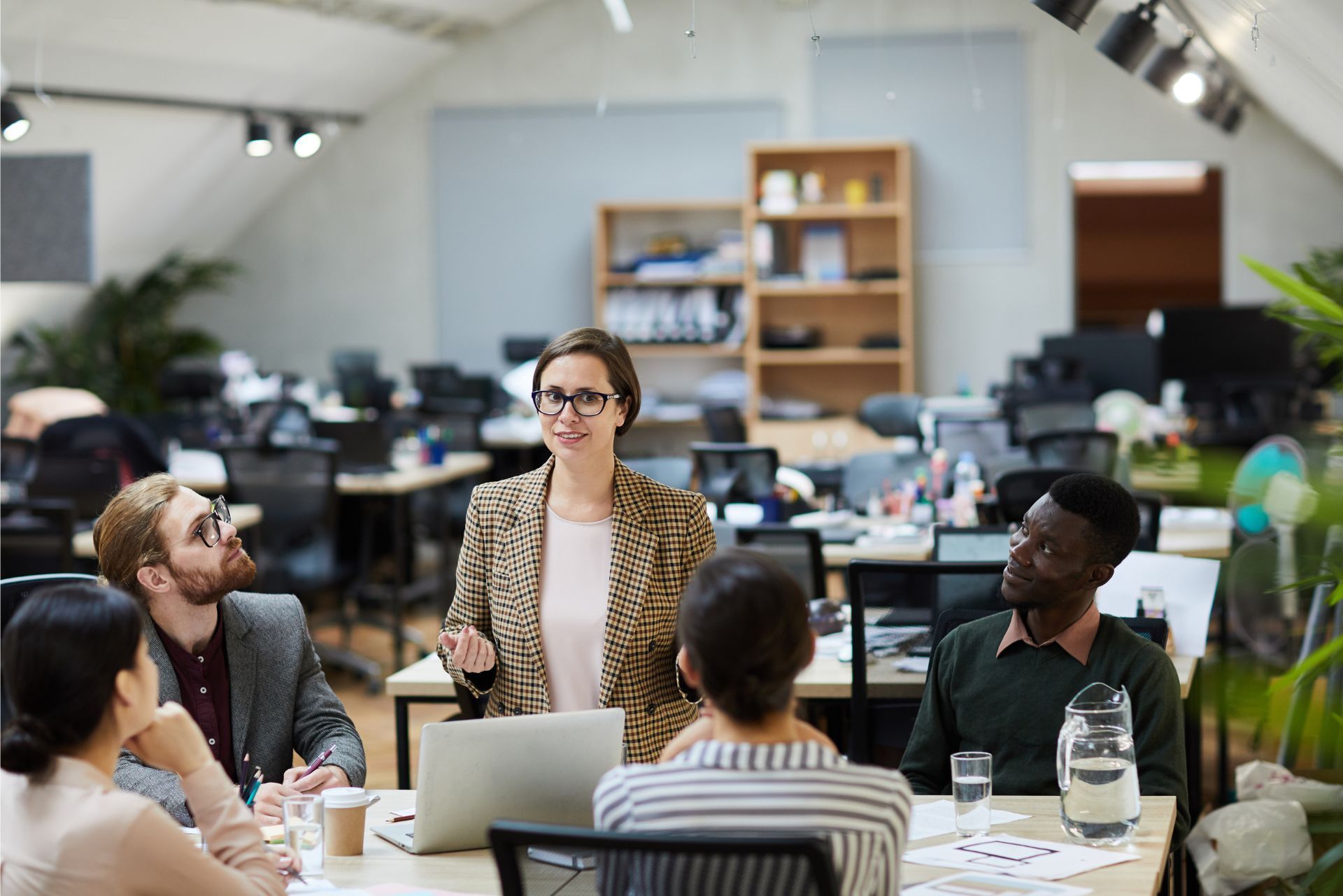 People meeting around a table in a bright office, with a woman standing and speaking.