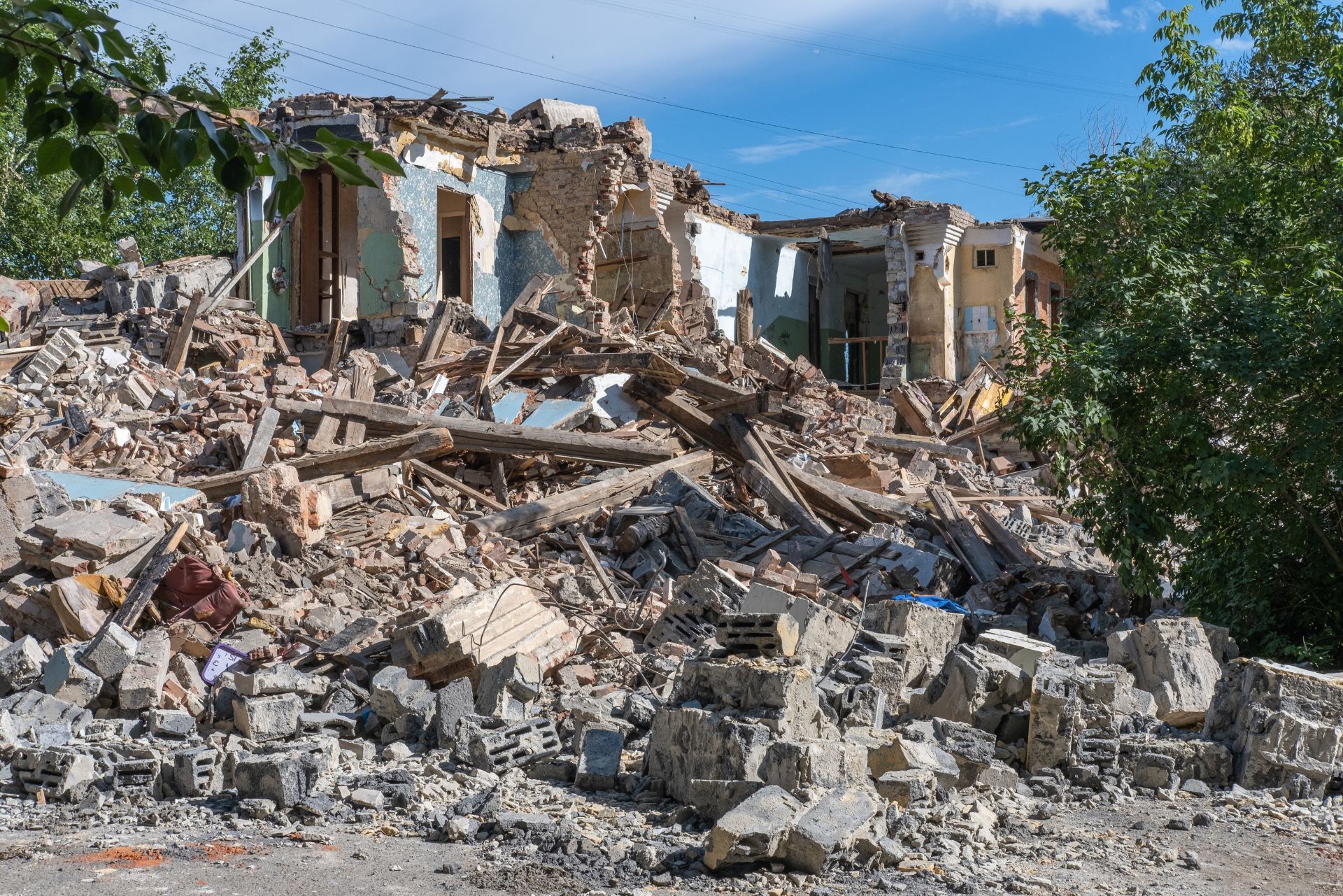 Collapsed building rubble and damaged houses amid debris under a blue sky