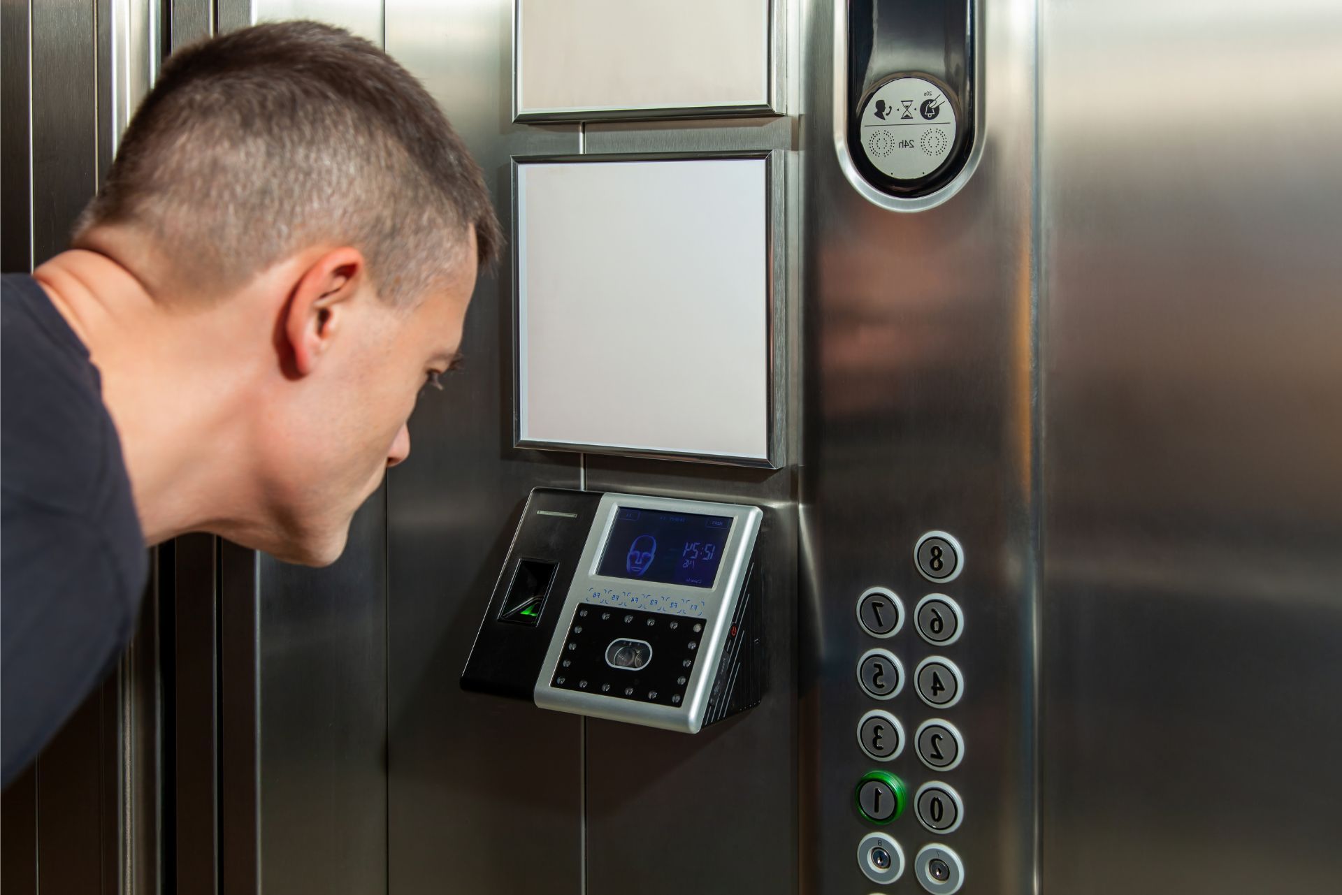 A person looking at a biometric scanner installed on a metallic elevator control panel with floor selection buttons.