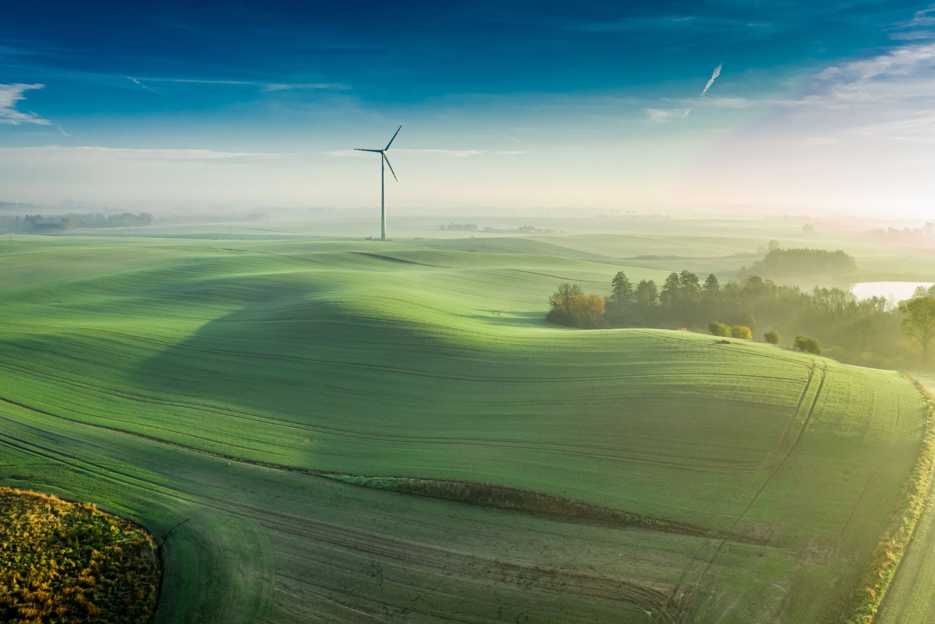 Rolling green hills with a wind turbine at sunrise under a blue sky