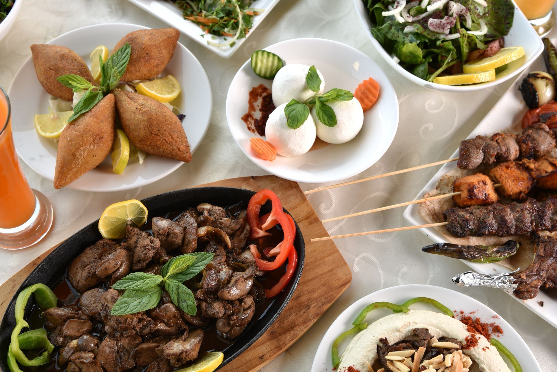 Assorted grilled meats and appetizers served on plates on a table, with herbs and vegetables.