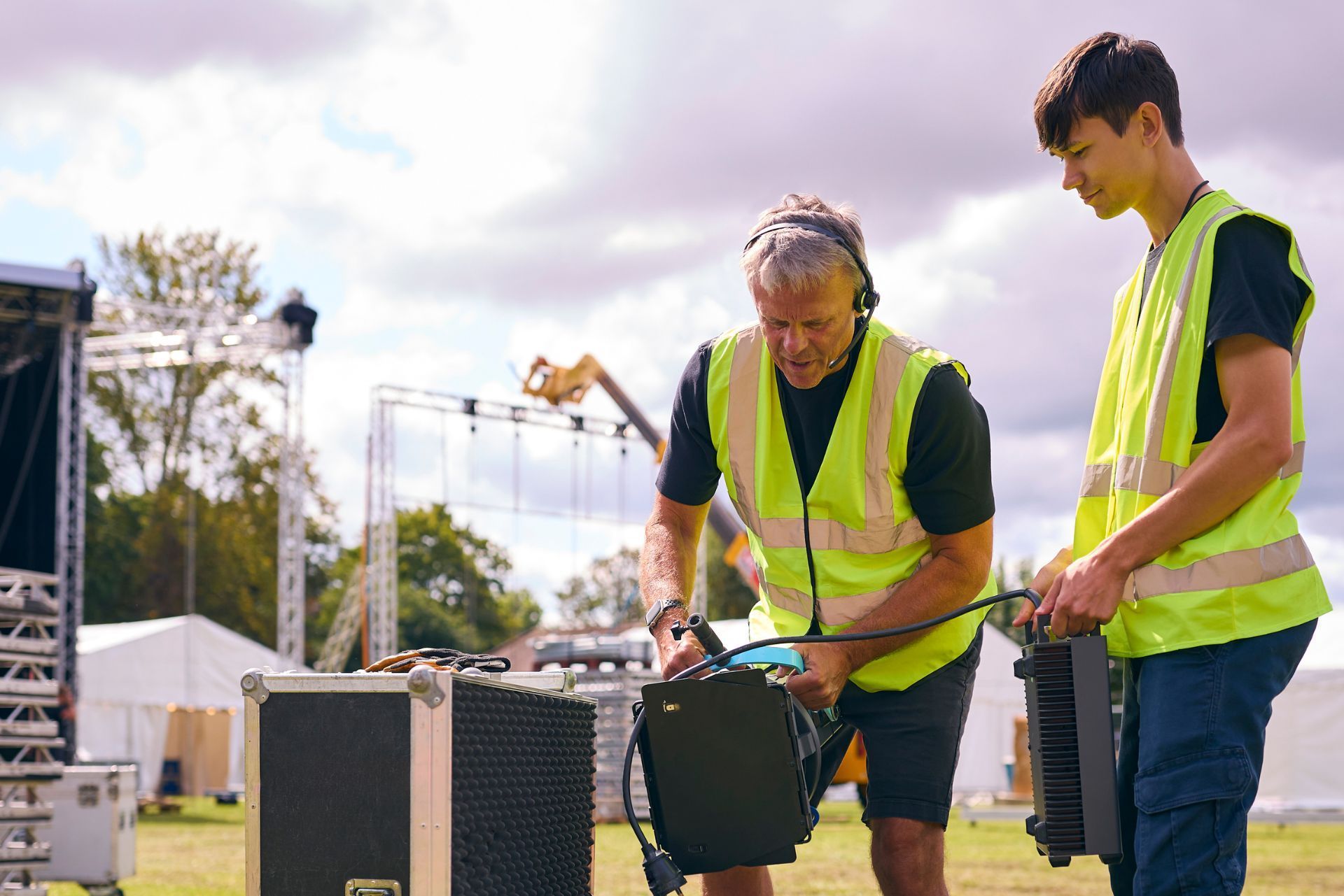 Two workers in neon safety vests handling equipment outdoors at a construction site