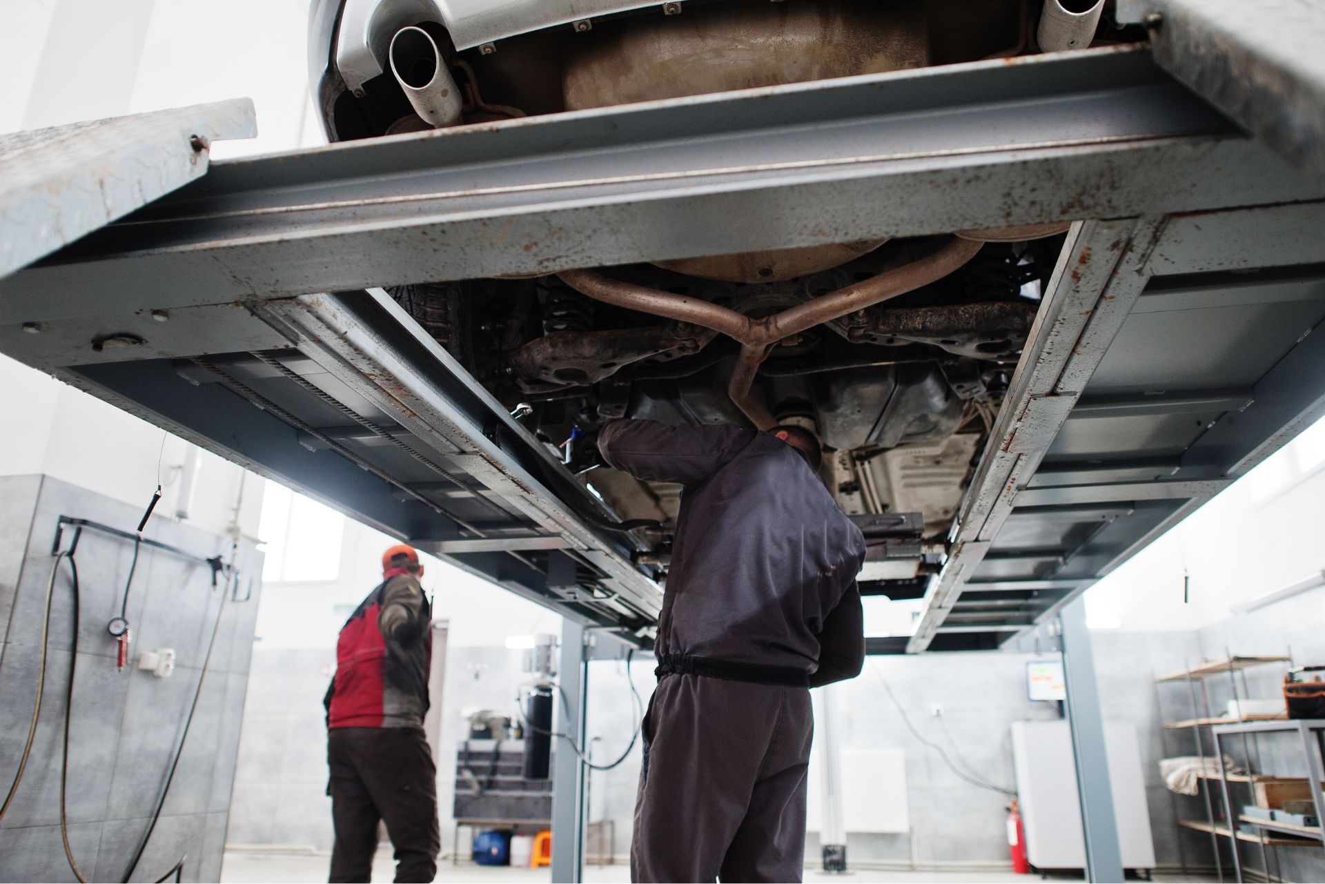 Mechanics inspecting the underside of a car in a garage lift, with tools and equipment nearby