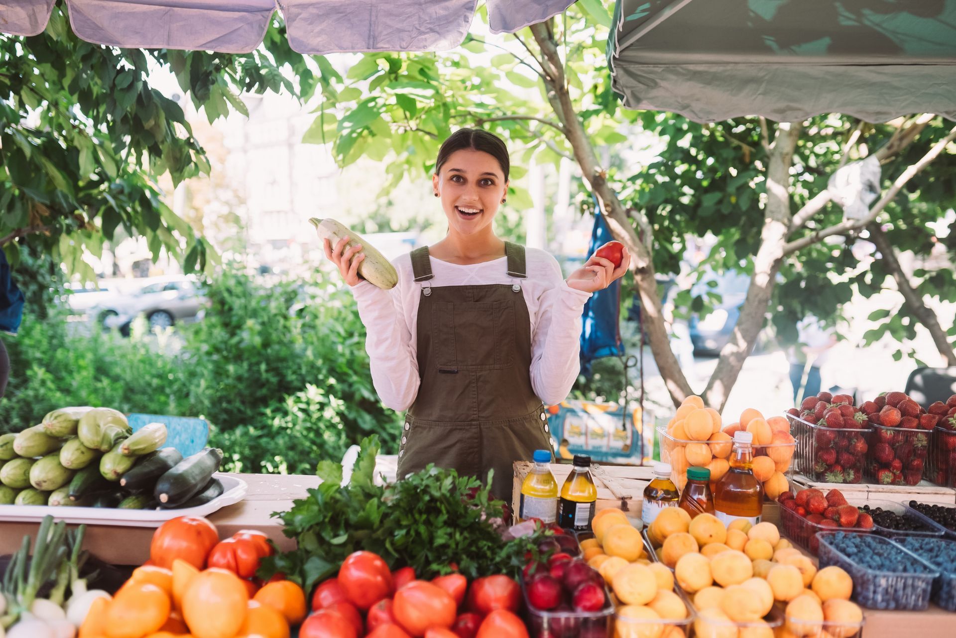 Vendor smiling at a colorful outdoor market stall with fresh fruits and vegetables