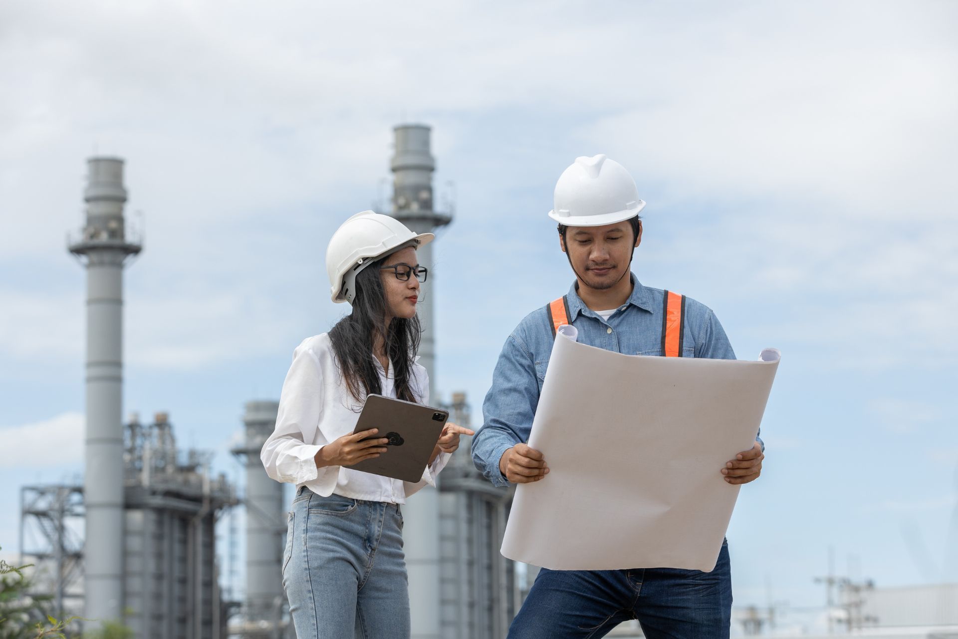 Two engineers in hard hats reviewing plans at an industrial plant