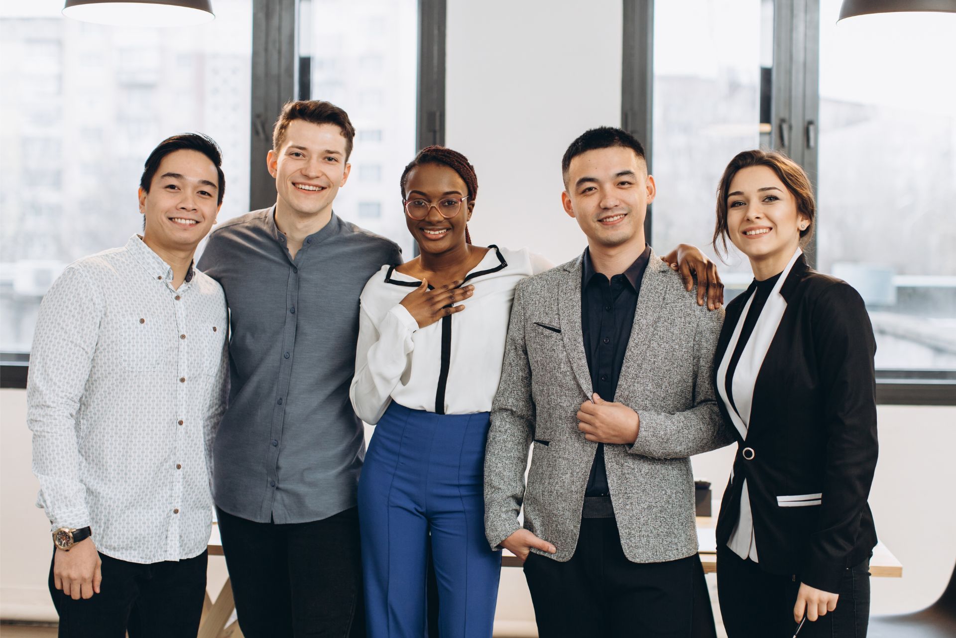 Five professionals standing together in a bright office, smiling and looking at the camera.