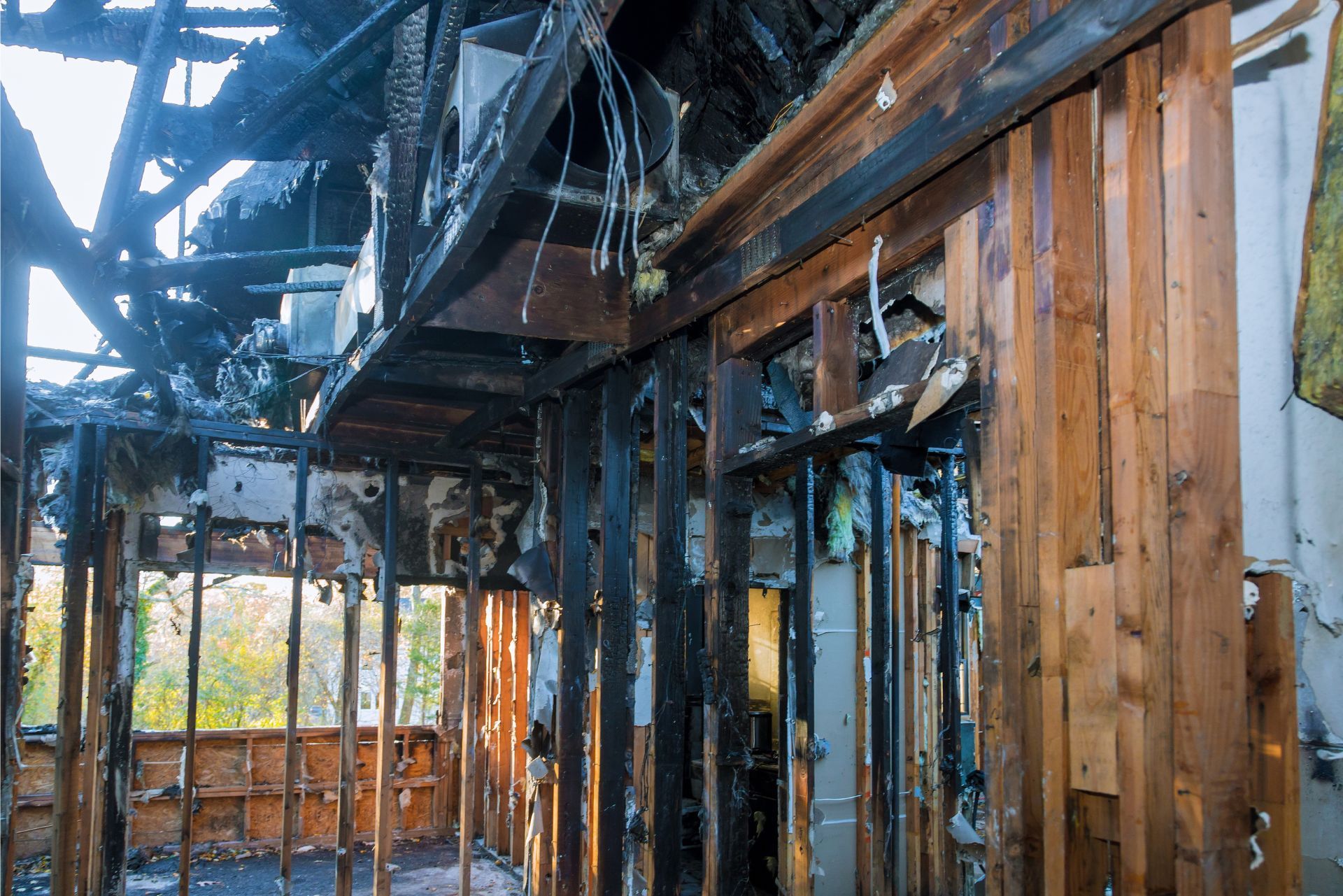 Interior view of a building heavily damaged by fire, showing charred wooden framing, blackened beams, and exposed studs.