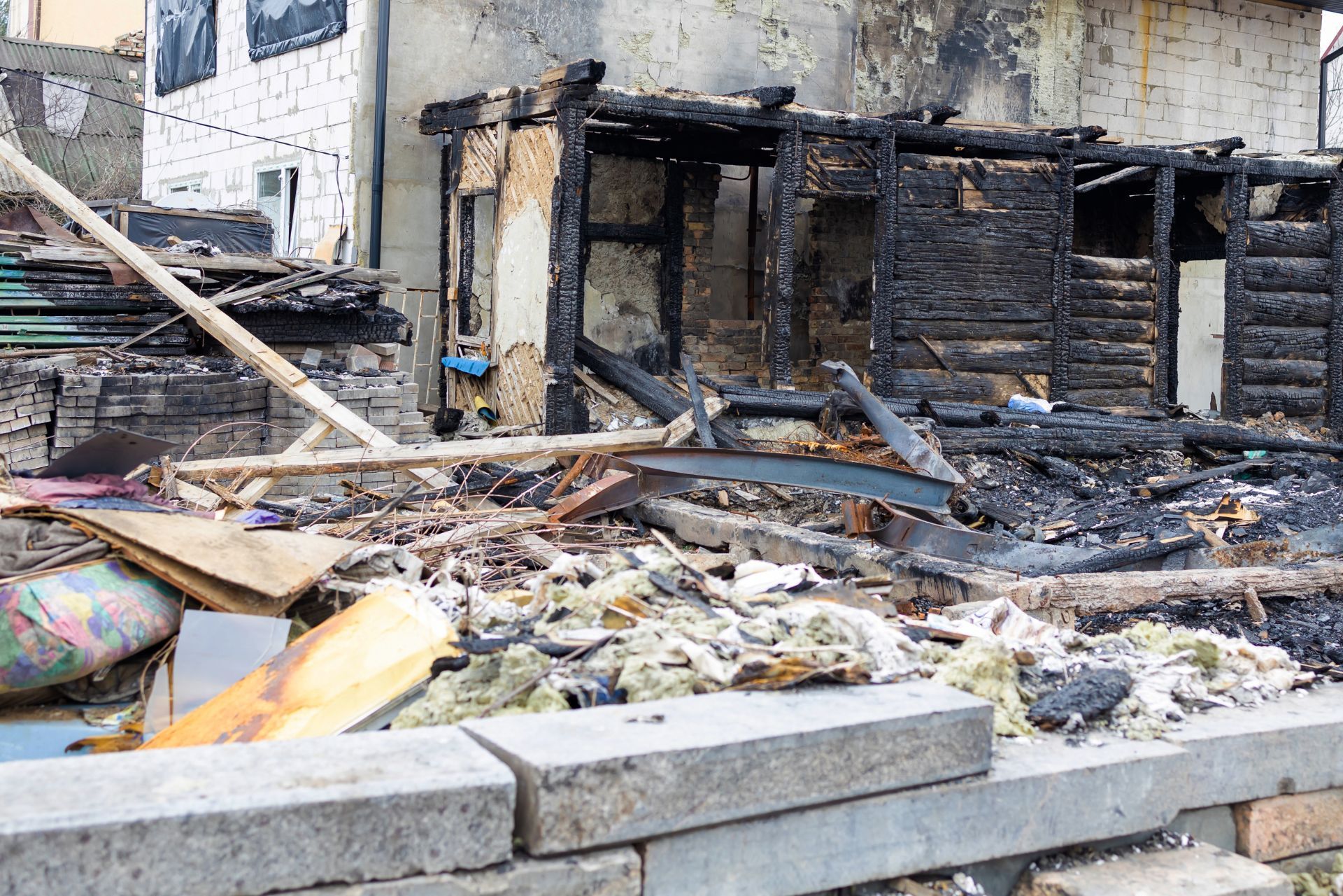 The charred, blackened remains of a partially destroyed wooden building in a residential setting.