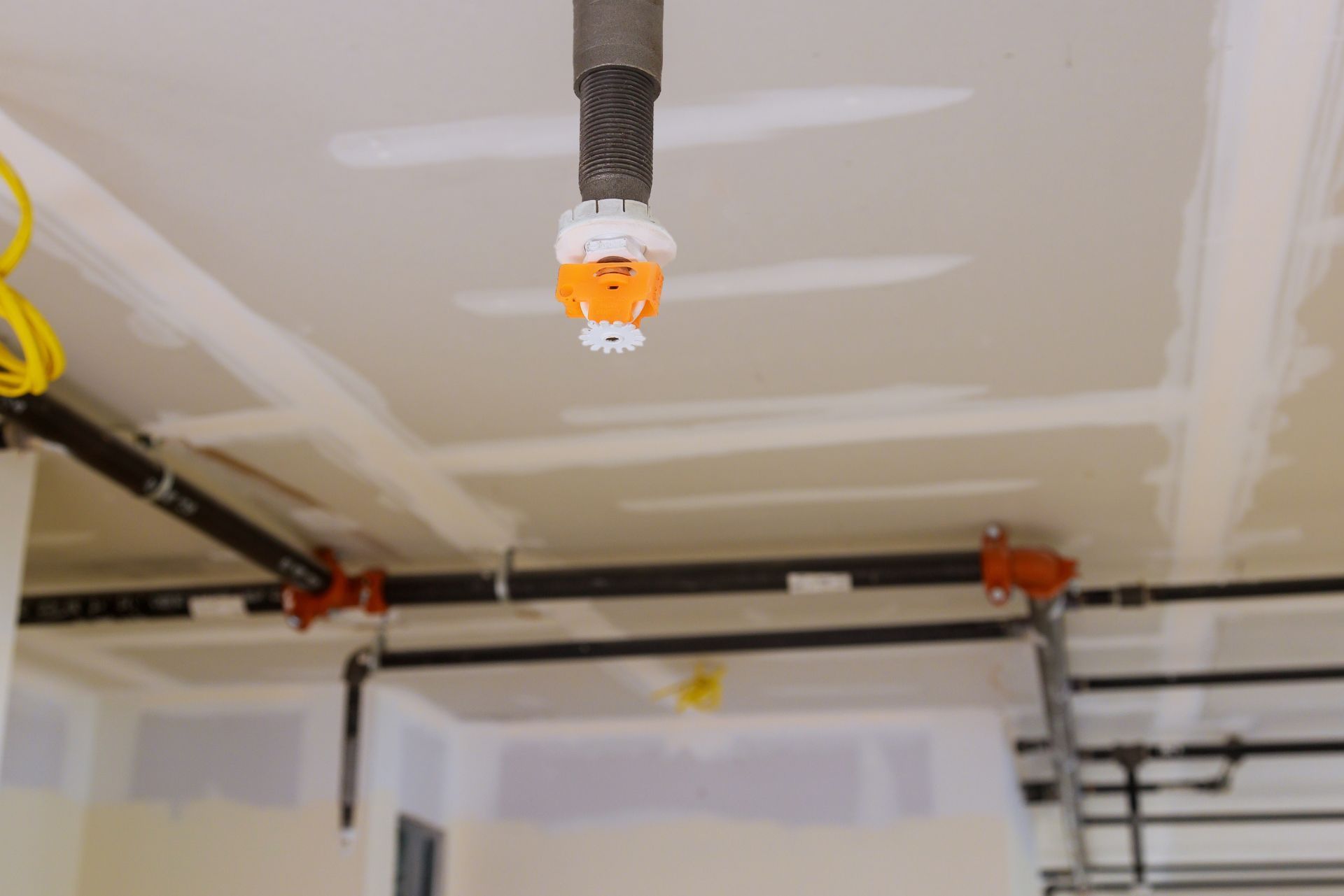 Ceiling-mounted sprinkler head in a garage, with black garage door tracks and taped drywall seams nearby