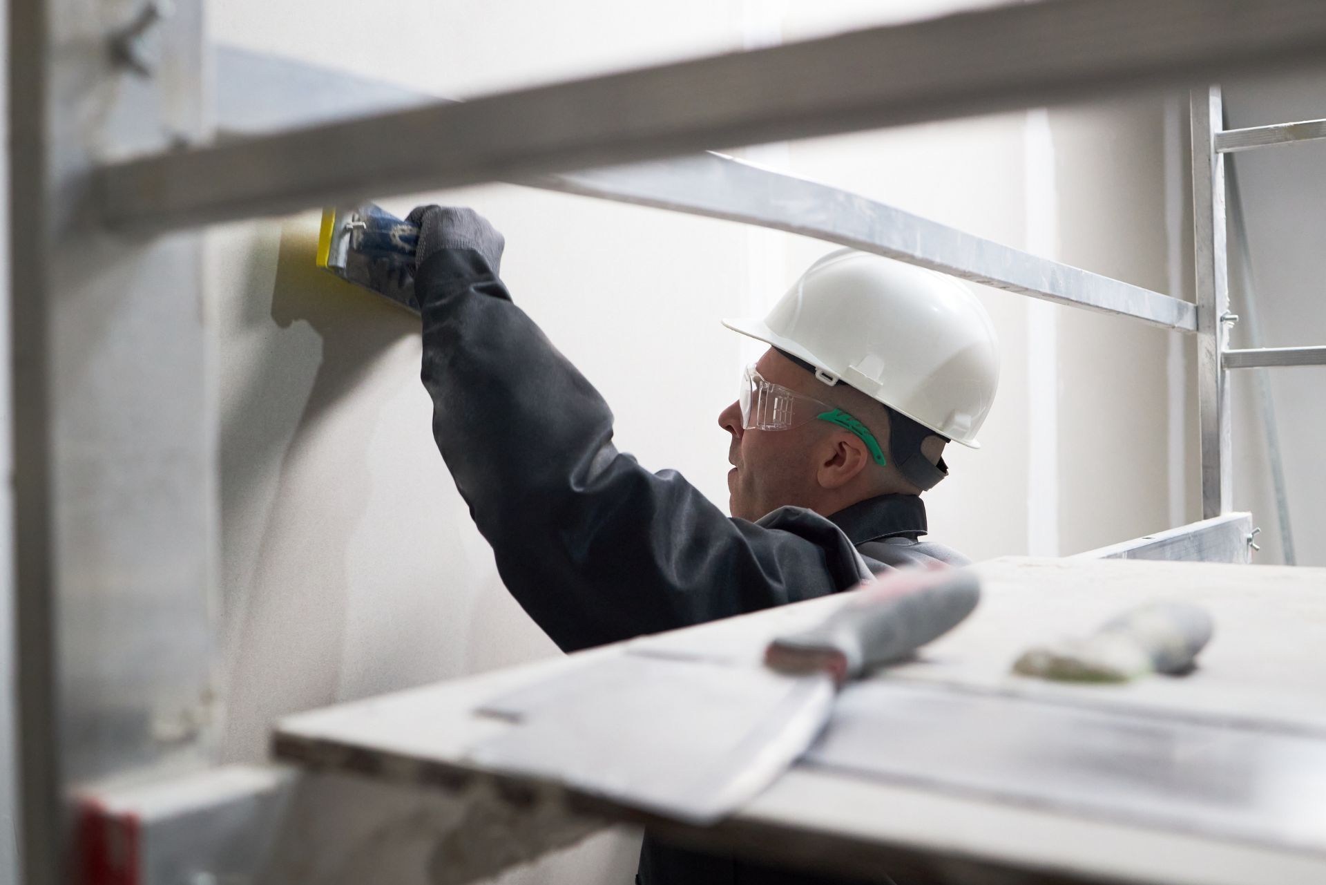 Worker in white hard hat drilling a wall in an industrial workspace