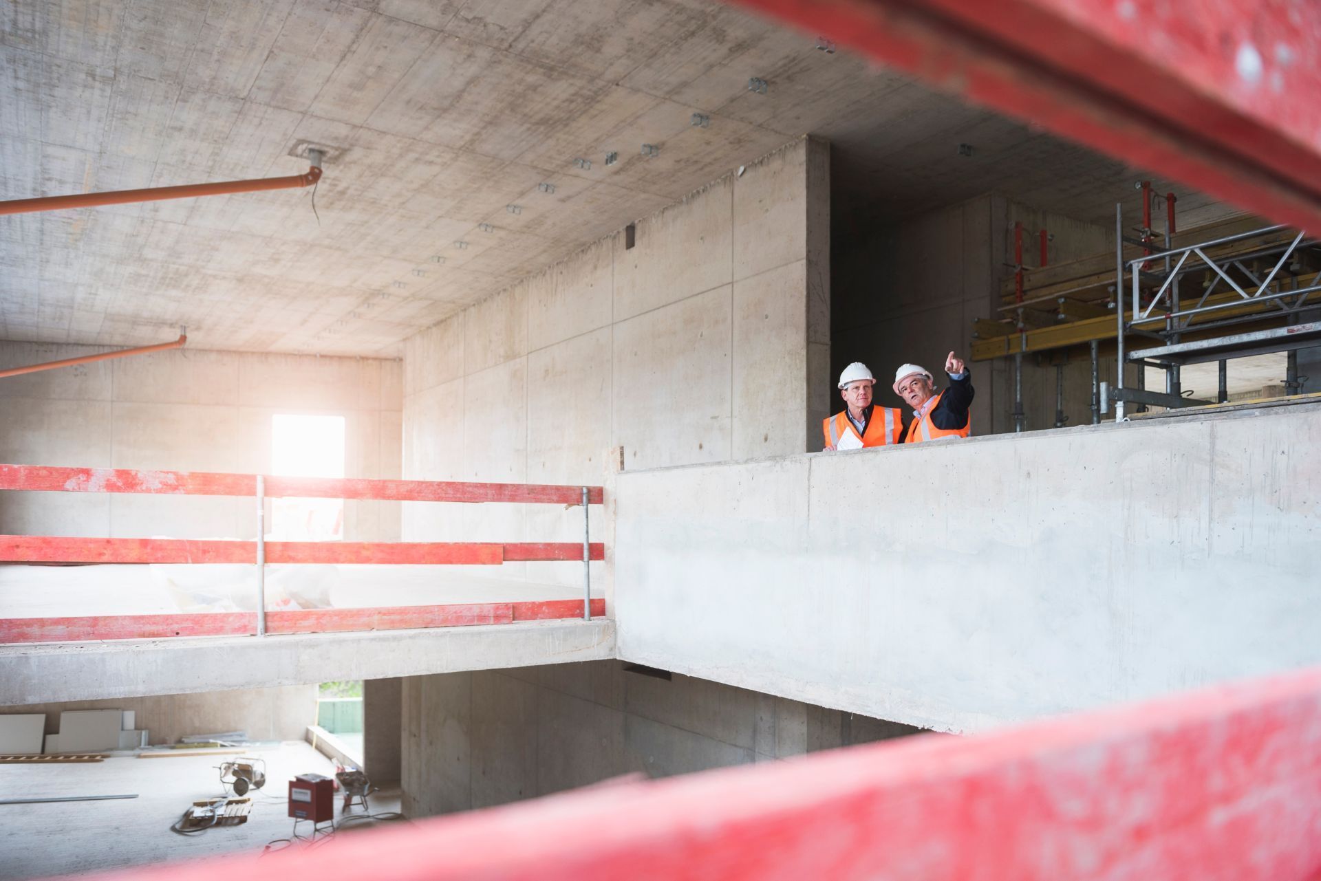 Construction site interior with two workers in orange helmets on a concrete mezzanine near scaffolding