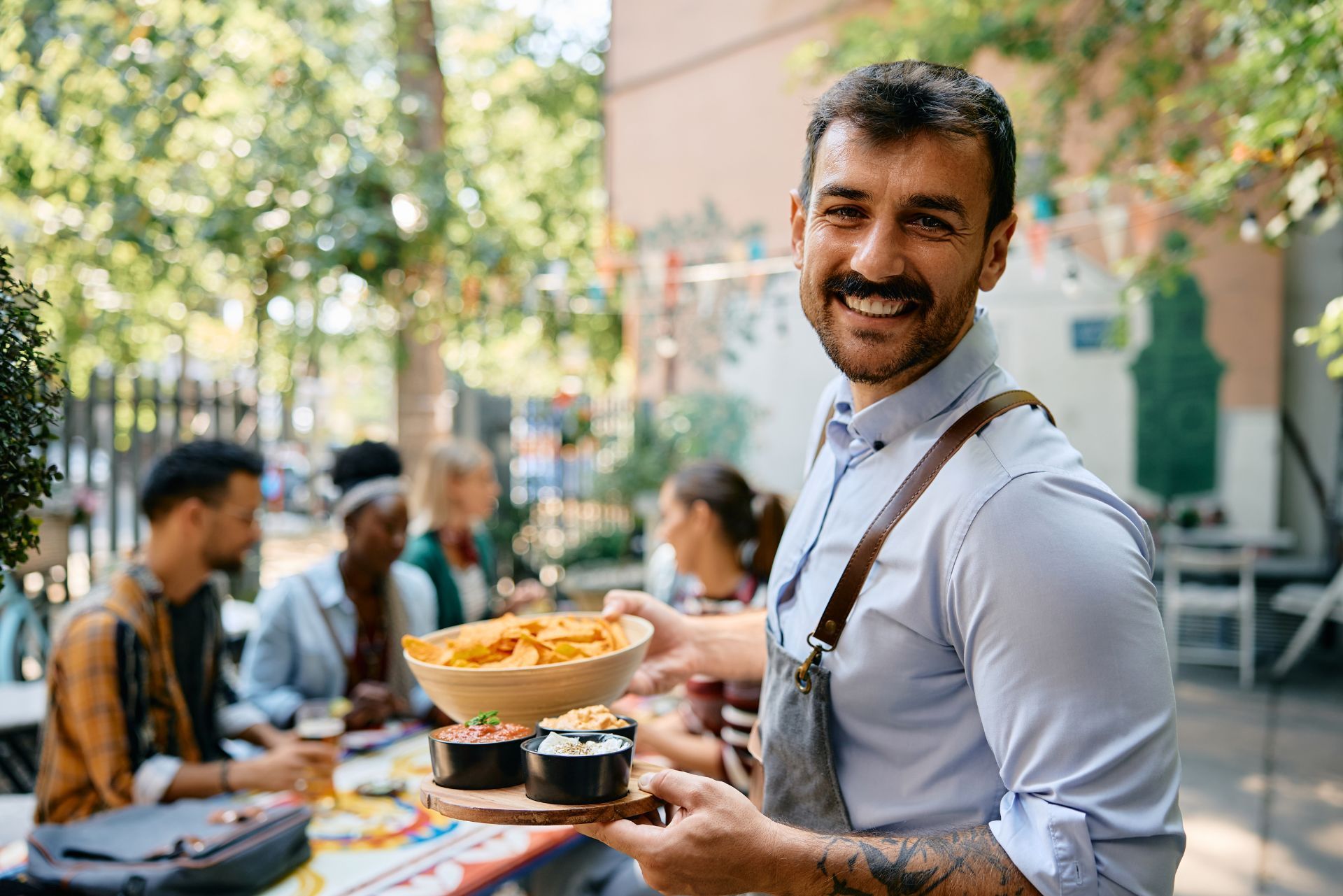 Smiling man serving food outdoors at a picnic table with friends in the background