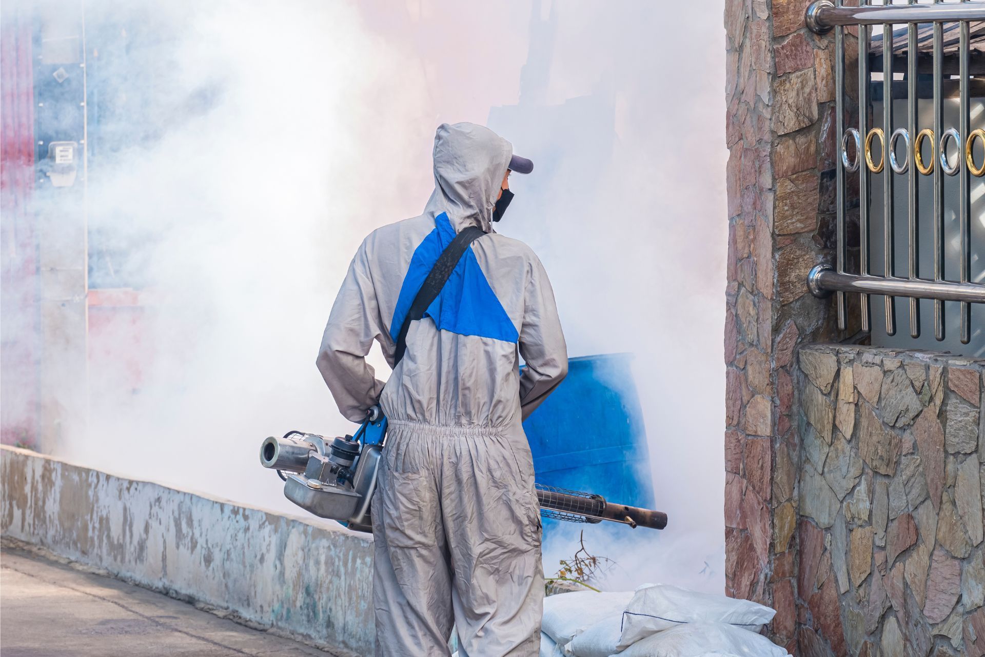 Worker in gray protective suit spraying blue paint on an exterior wall beside a doorway