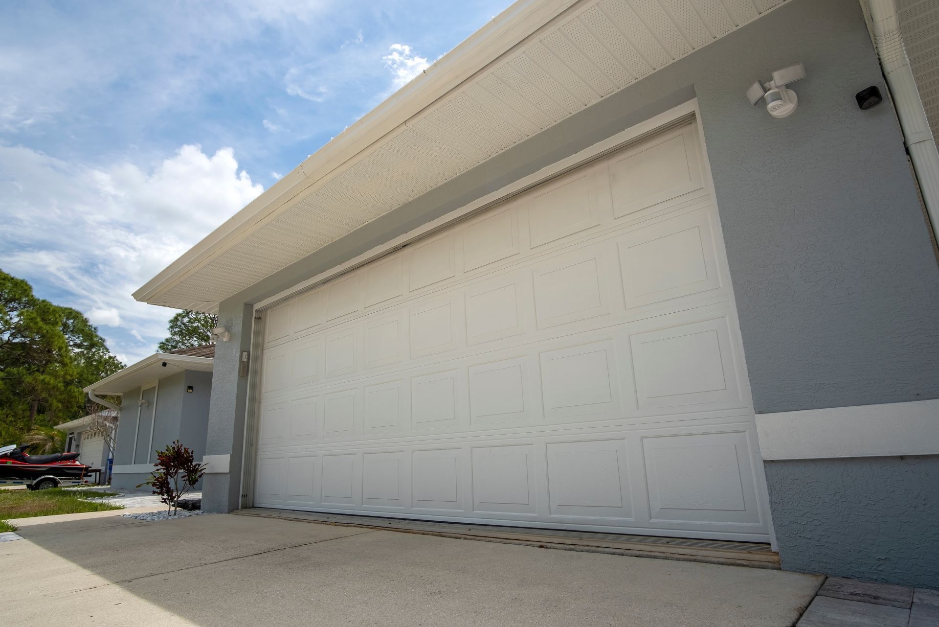 White garage door on a gray house under a bright blue sky.