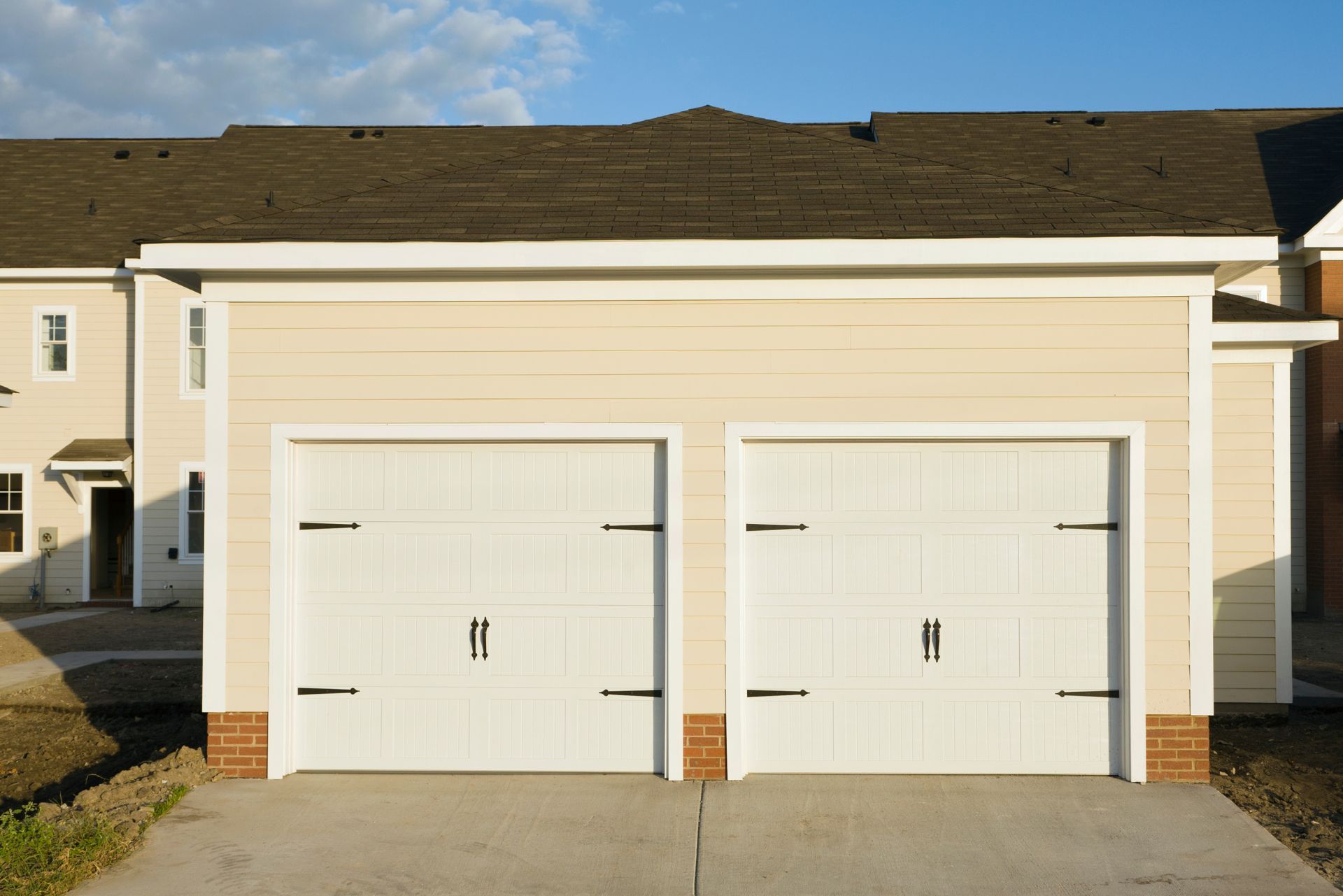 Two white garage doors on a beige house with brown roof and driveway