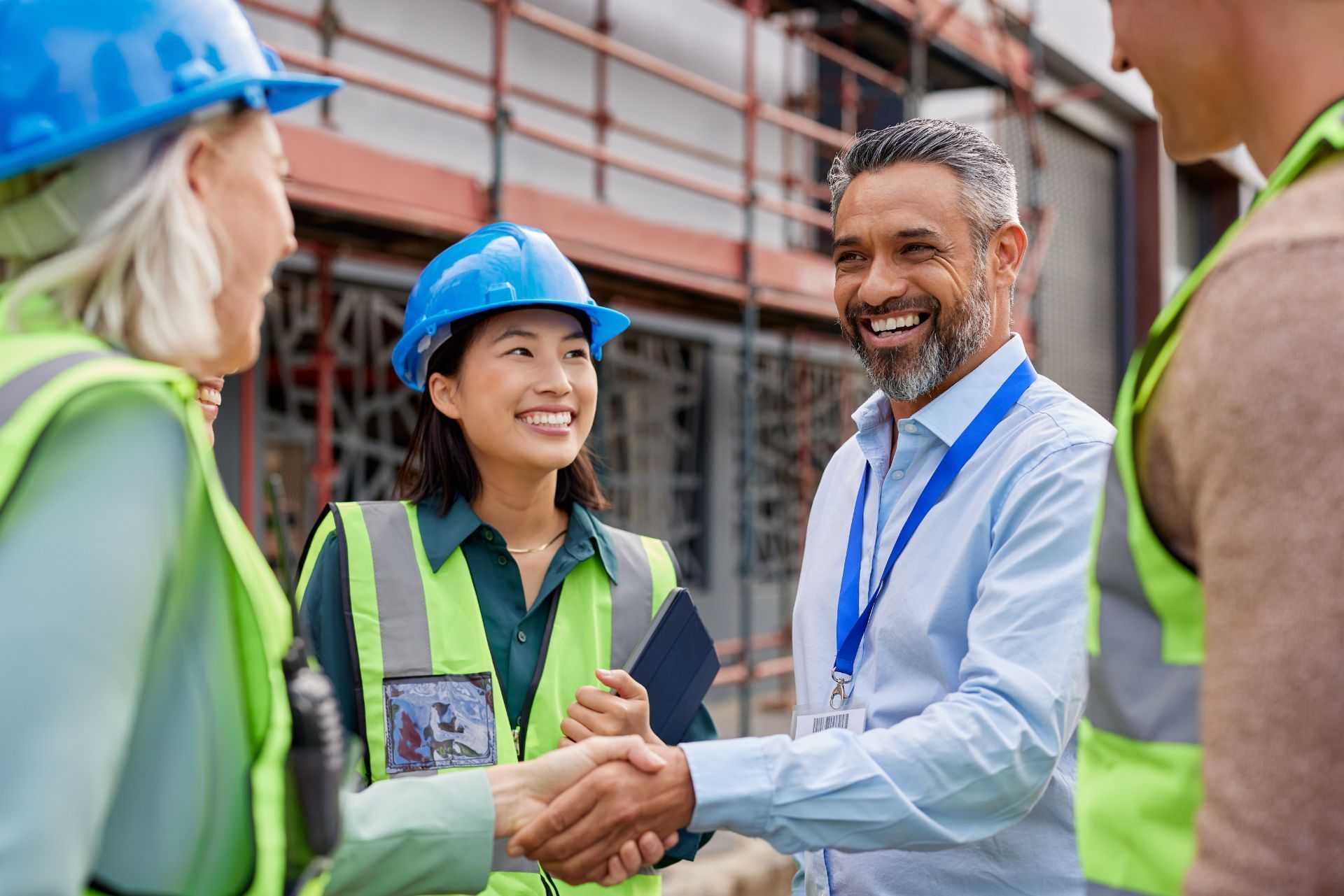 Construction workers in high-visibility vests and blue hard hats shake hands on a building site.