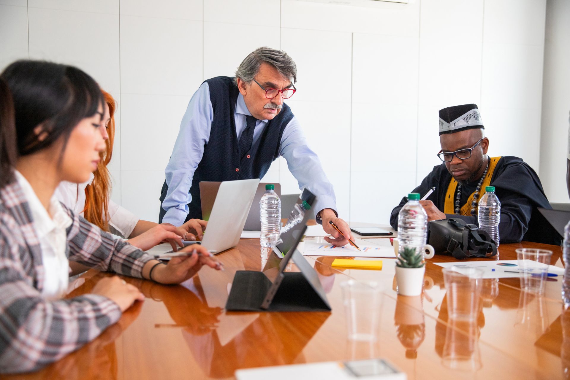 People collaborating in a meeting around a wooden conference table with laptops and papers