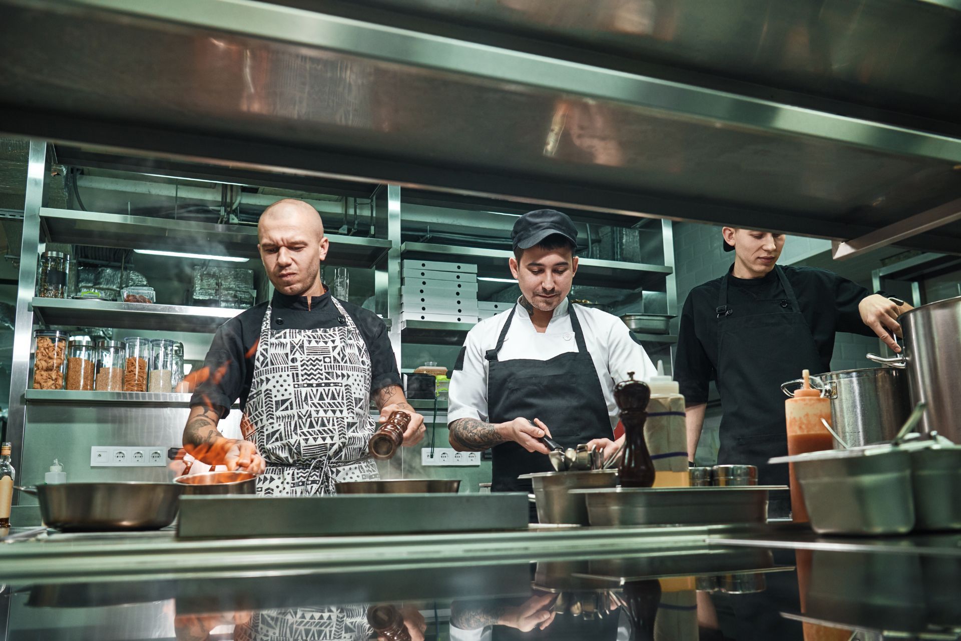 Three chefs in a professional kitchen cooking at a stainless steel station.