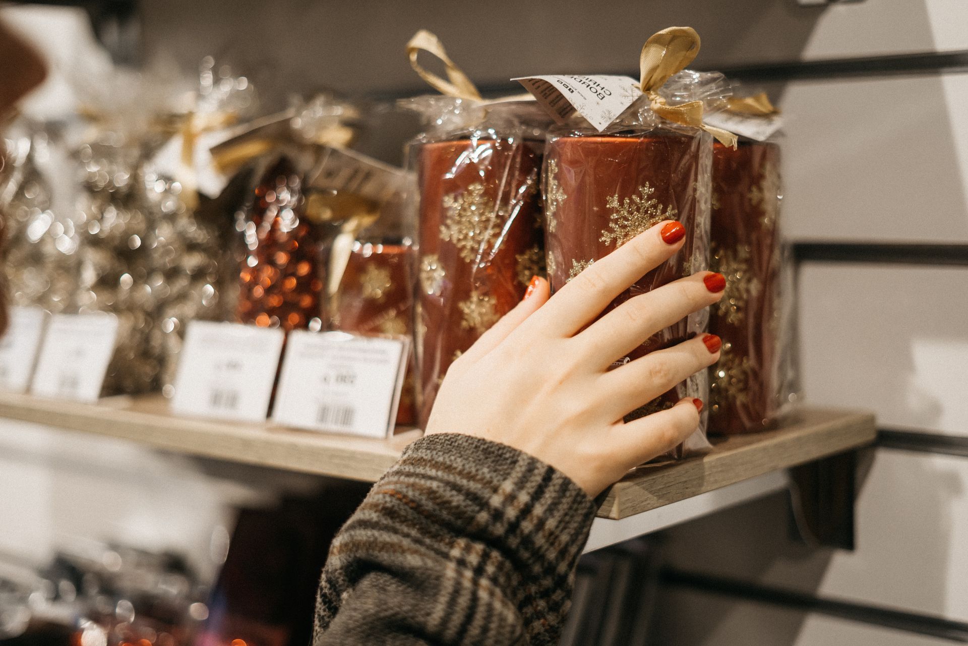 Hand reaching for red gift jars on a store shelf, wrapped in clear cellophane and ribbon