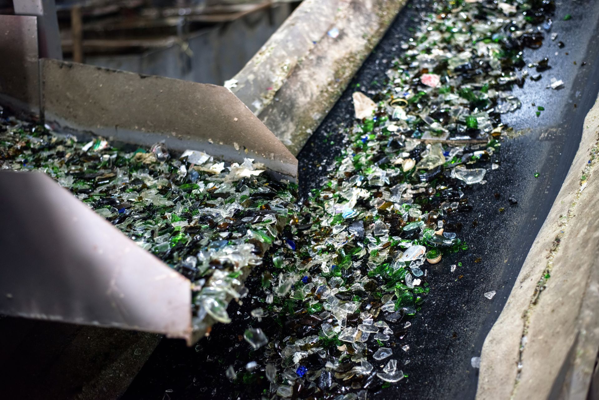 Broken shards of glass travel along an industrial conveyor belt at a recycling facility.