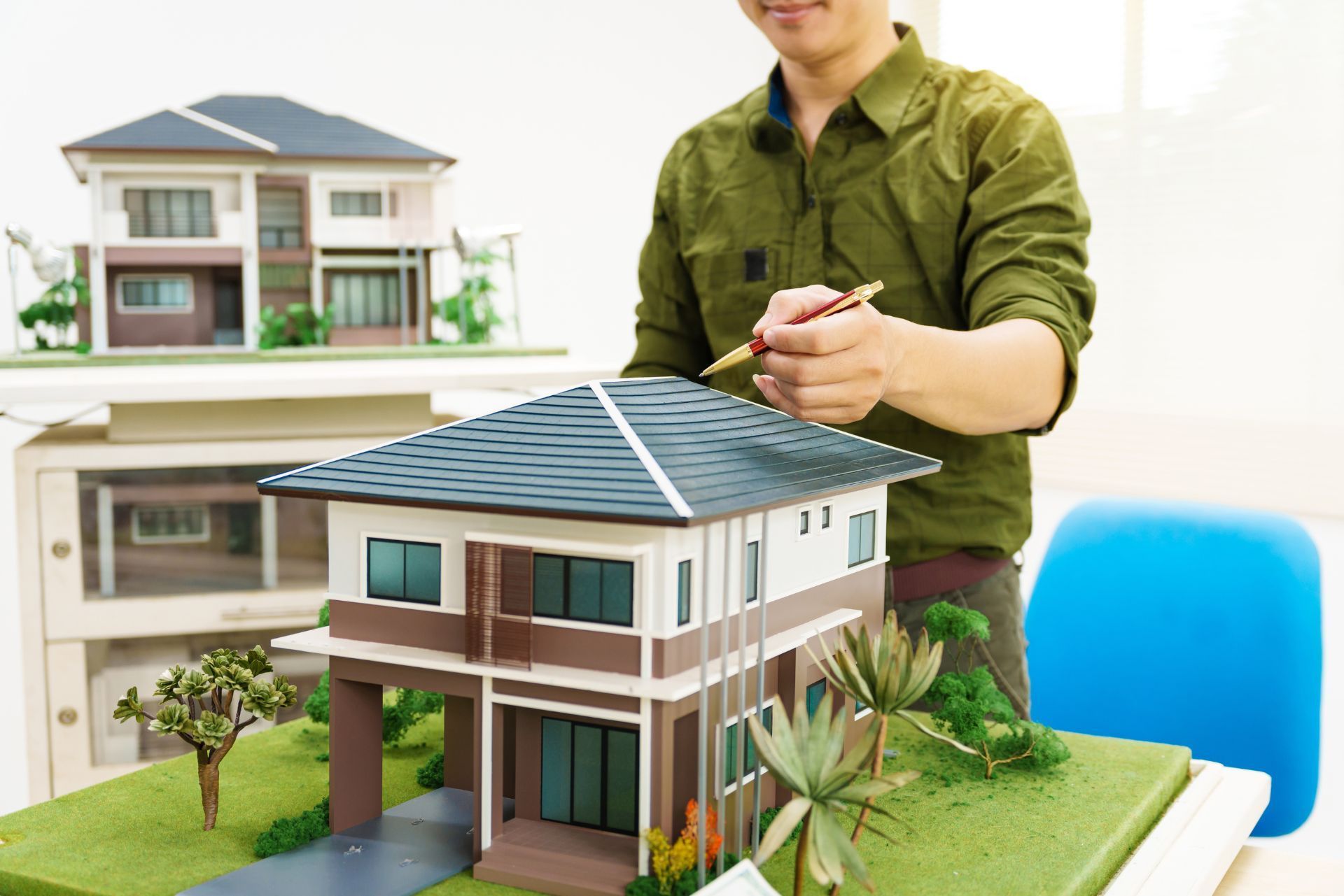 Person building a detailed model house beside a larger house model on a desk