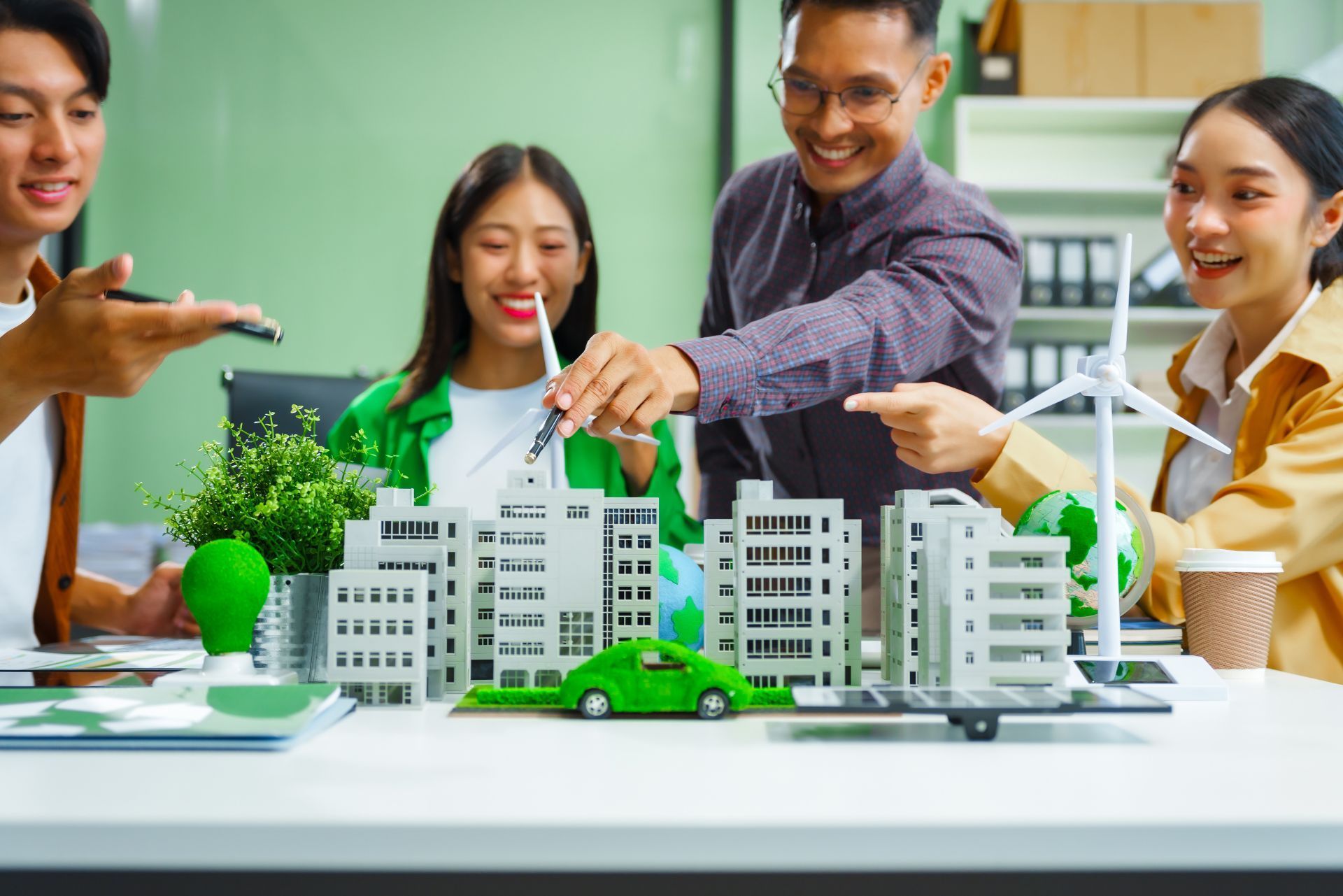People building a miniature city model together at a table, with cars, trees, and smiling faces