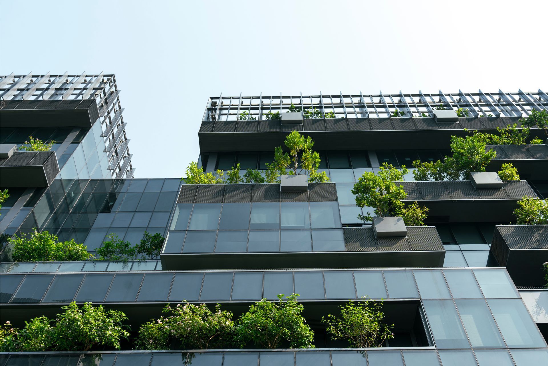 Modern dark-gray building facade with glass panels and lush green rooftop planters